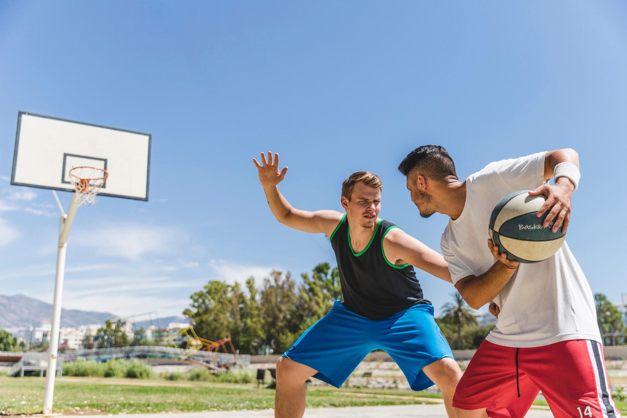 Two men on a basketball court, one dribbling the ball and the other ready to make a defensive move.  