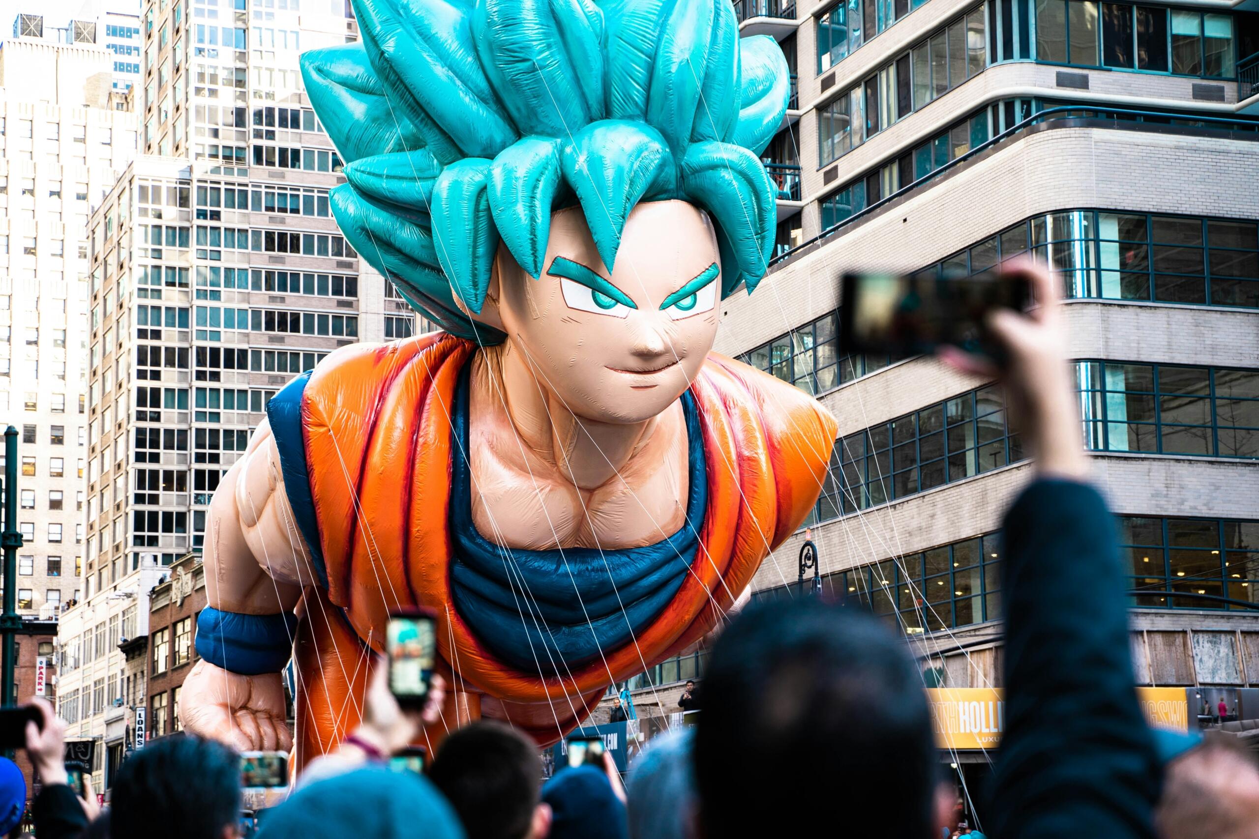 A large inflatable balloon of Goku, a Dragon Ball Z character, being photographed by people in a square.