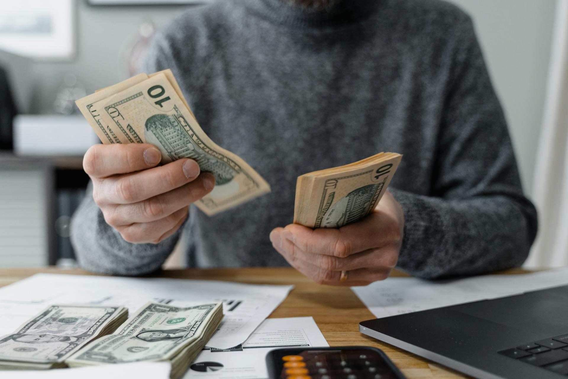 A man holds cash in front of a laptop, suggesting a financial transaction or online business activity.