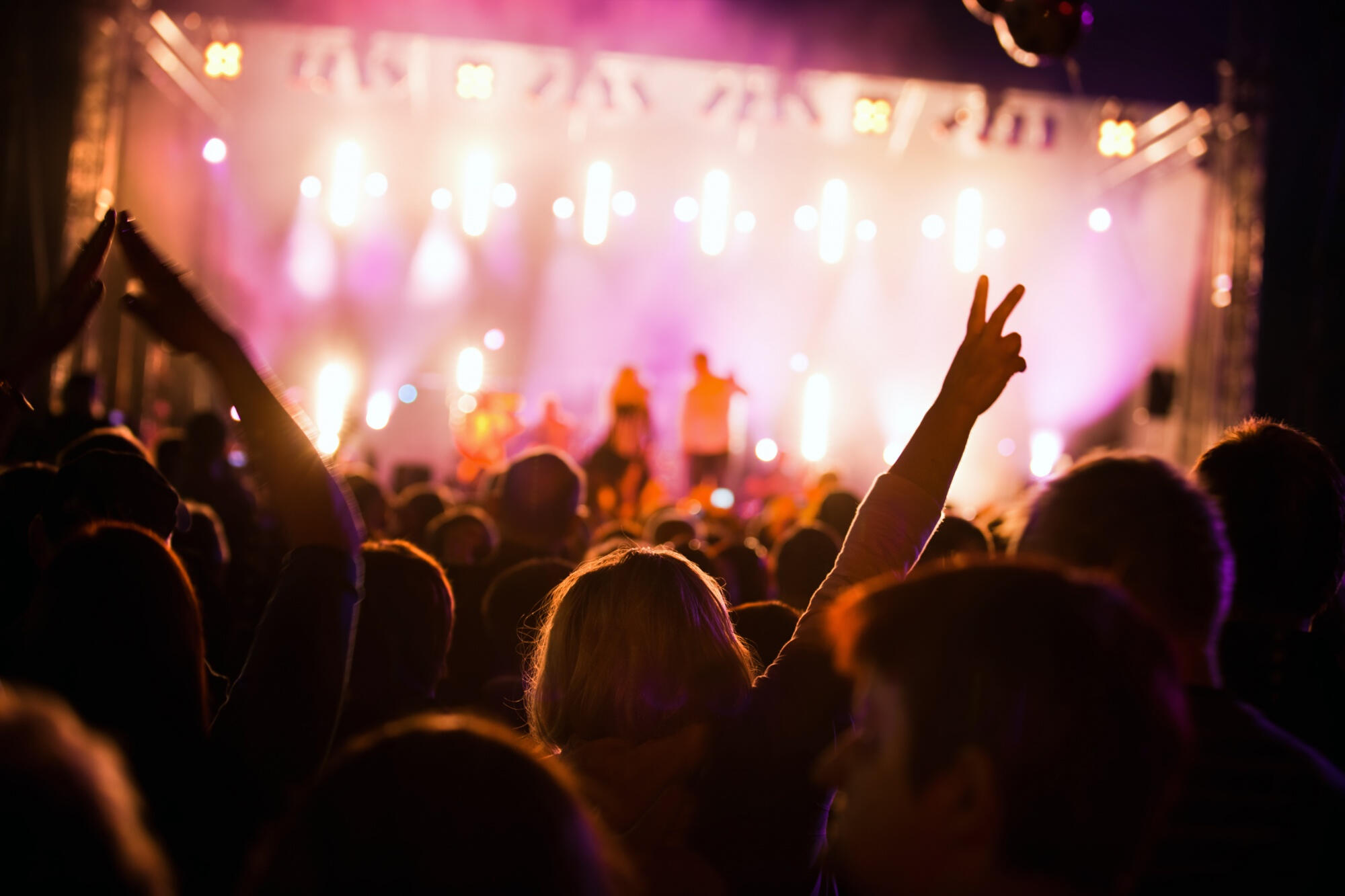 A lively concert crowd with people enthusiastically raising their hands in the air, enjoying the music together.  