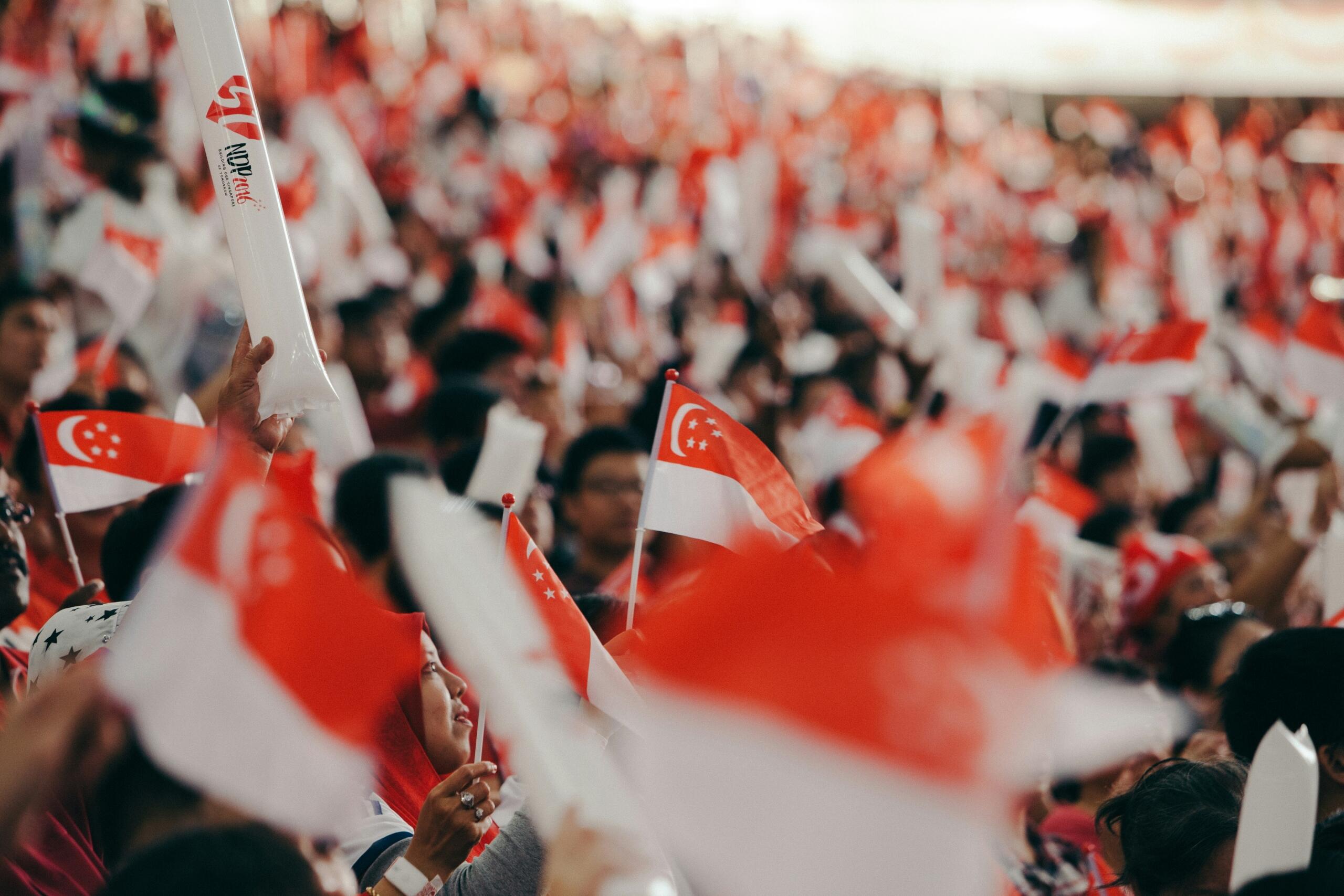 People in red and white shirts in a huge gathering, all waving small Singaporean flags.