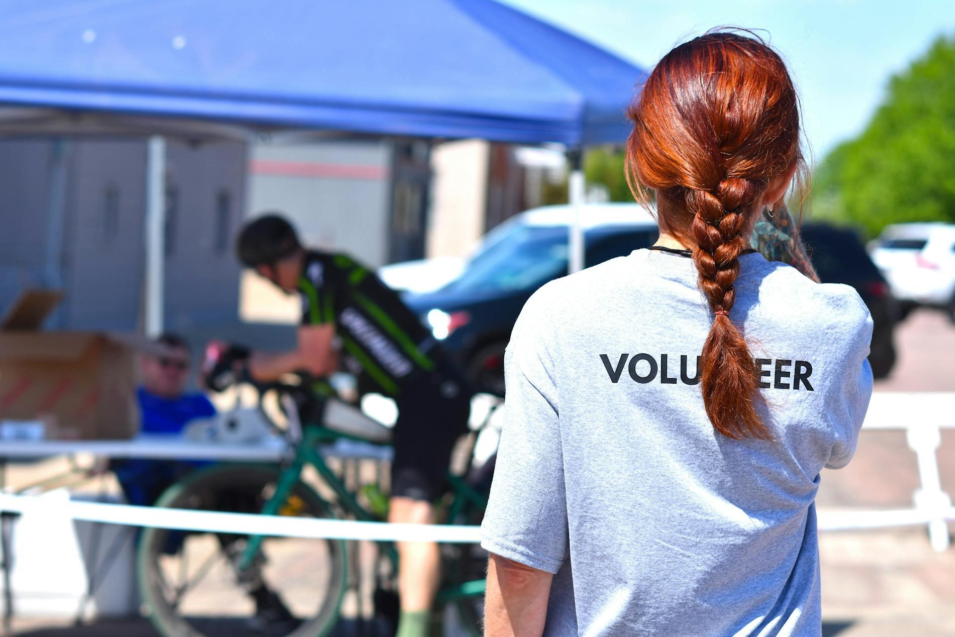 A volunteer oversees a charity bike event under a blue tent on a sunny day