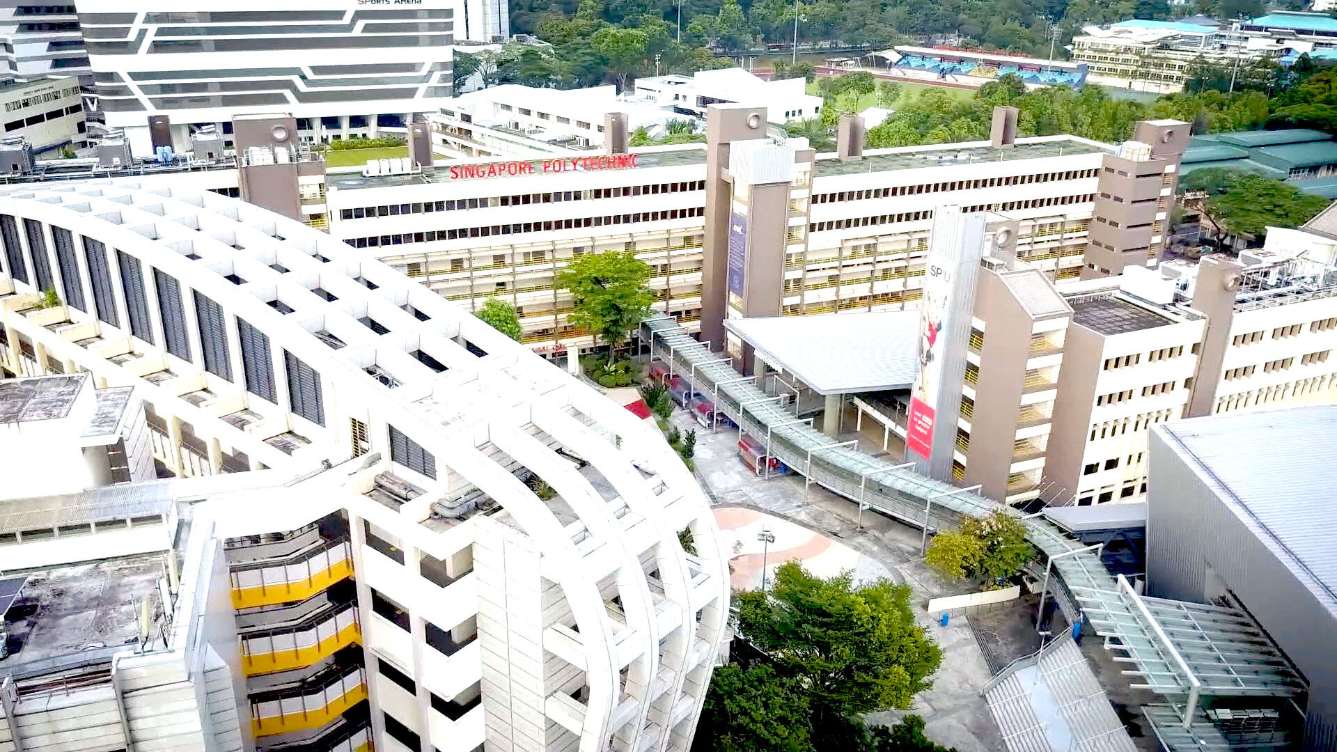 Aerial view of a modern urban landscape with a mix of buildings, including some with distinct architectural designs, surrounded by greenery and pathways.