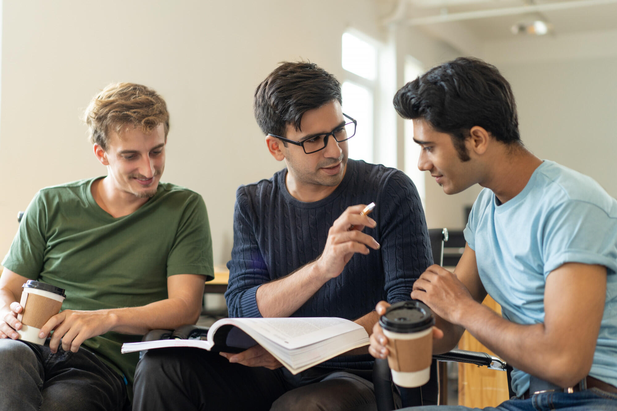 Three men are seated on a couch, each with a book and a cup of coffee, sharing a moment of leisure.  