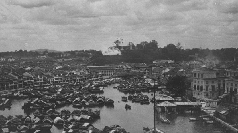 A black and white image depicting a port in Singapore during the 19th century, bustling with crowded docks and boats.