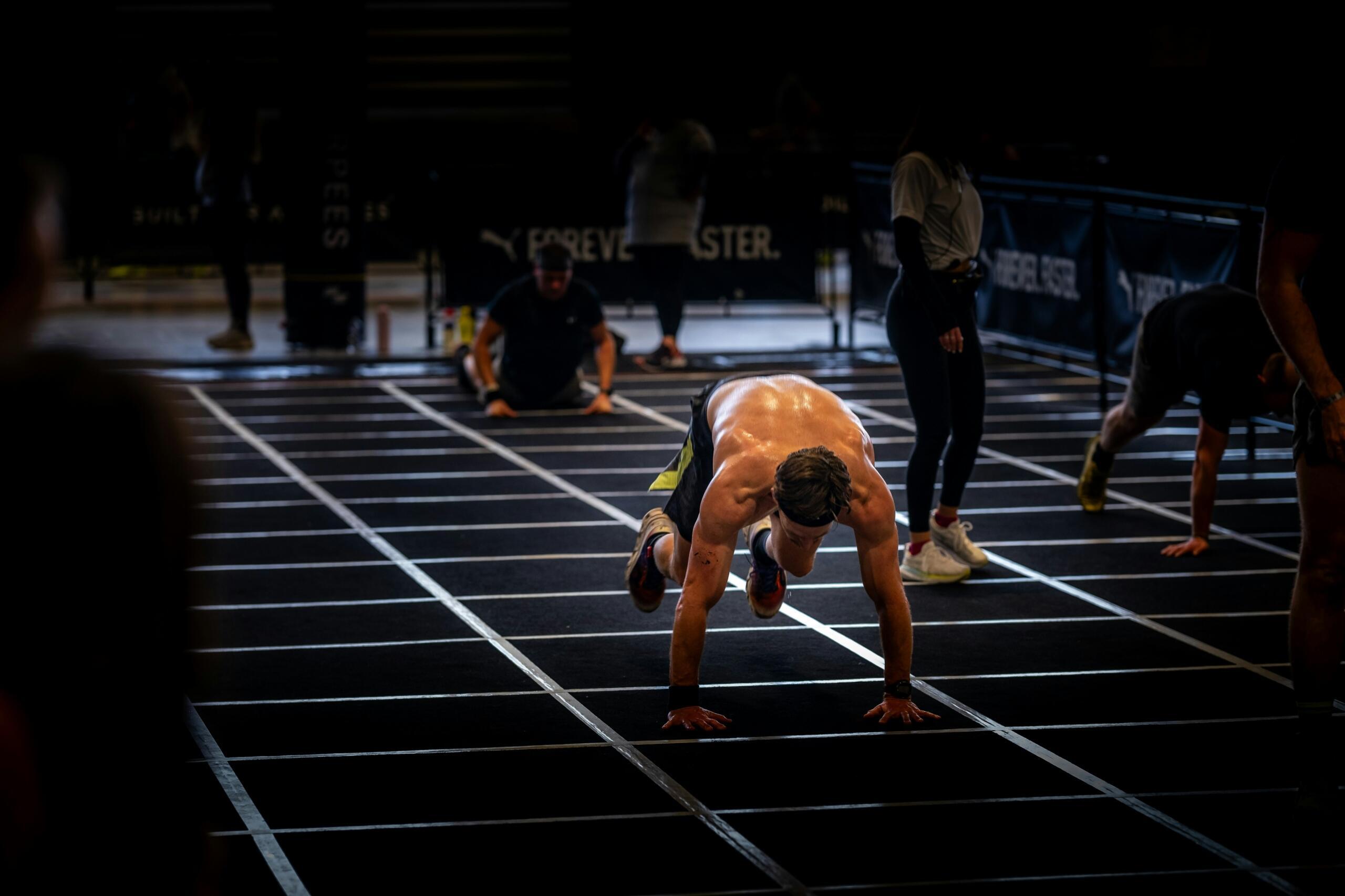 An athlete doing burpees on a floor mat at a HYROX event.