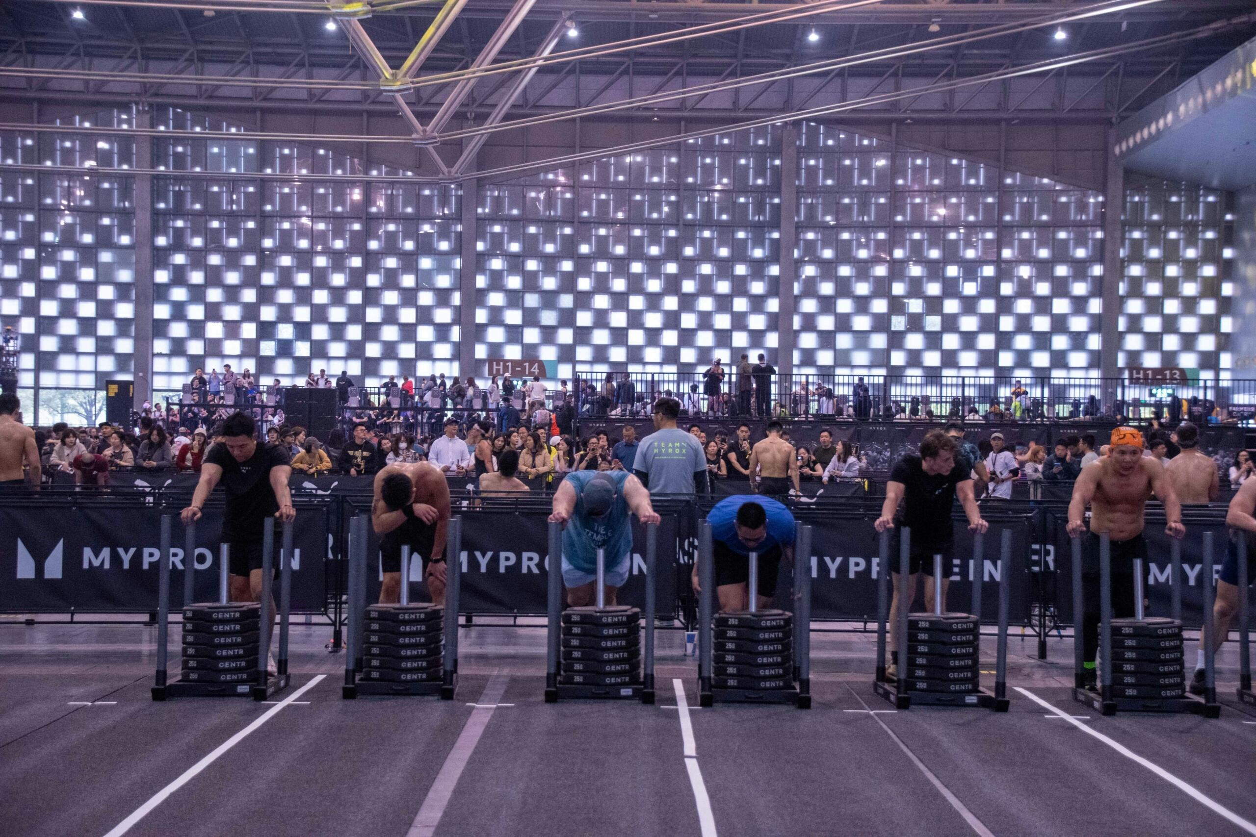 Athletes compete in a HYROX event by pushing weighted sleds indoors.
