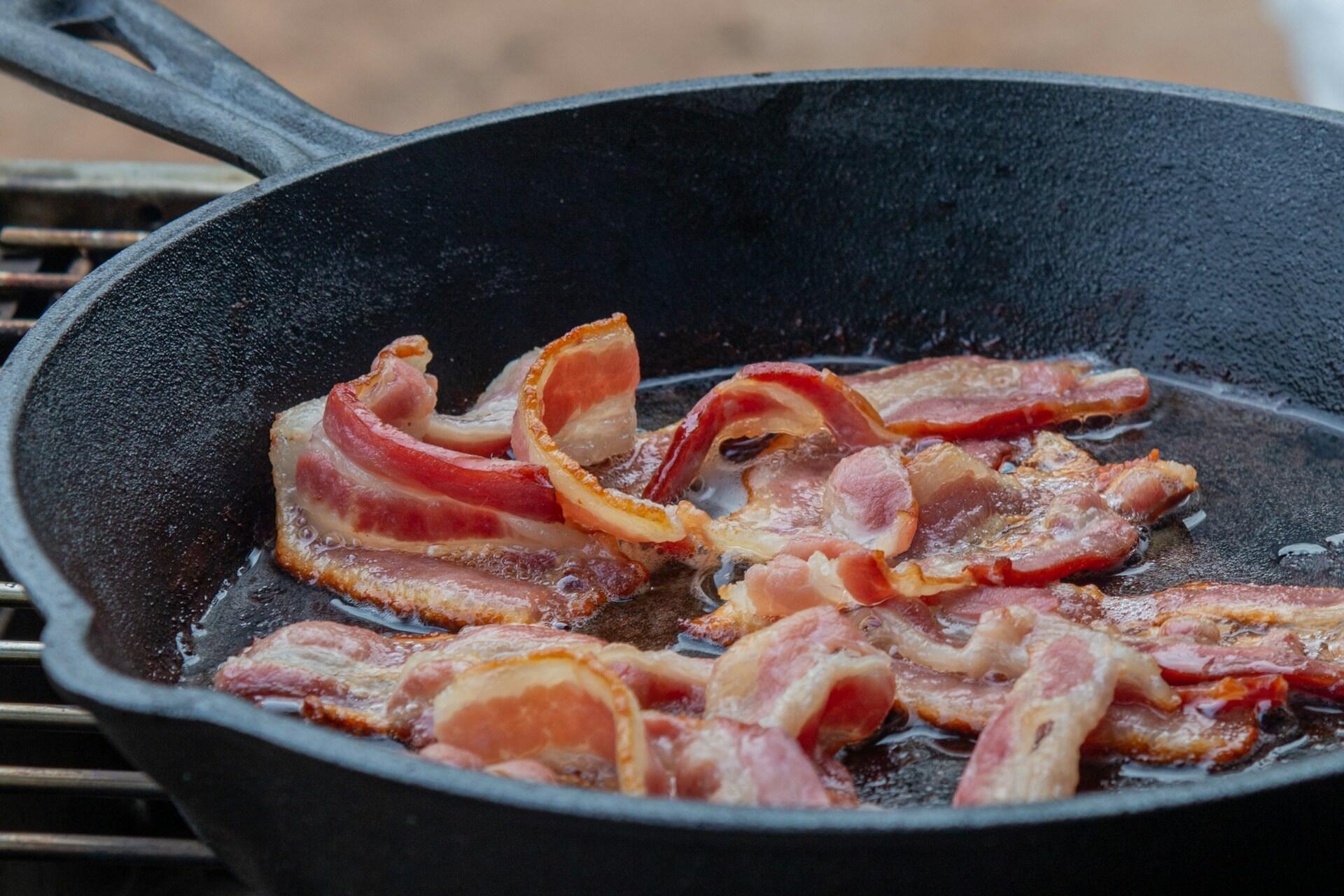 Strips of bacon cooking in a black frying pan