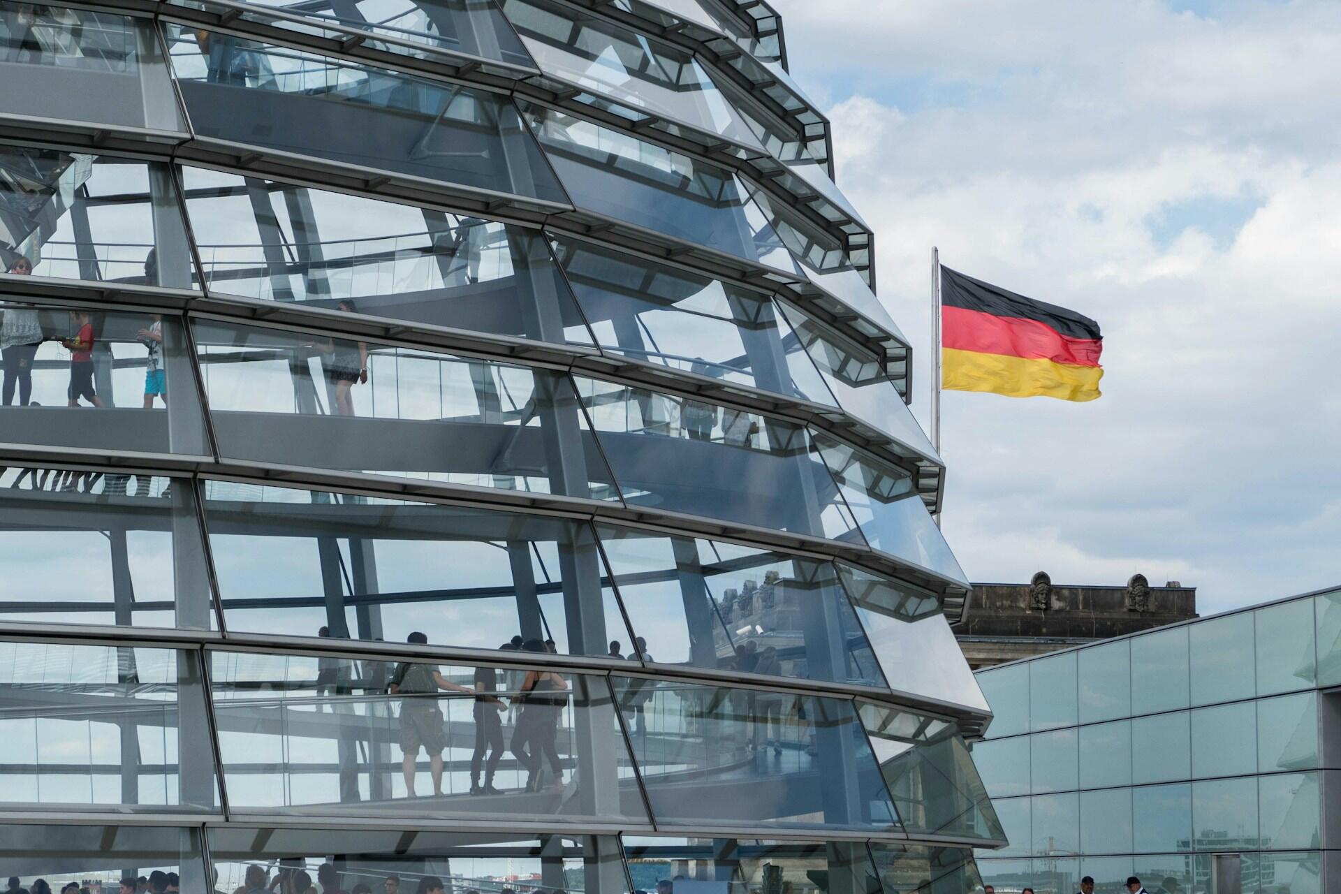 German flag beside a glass building under a cloudy sky