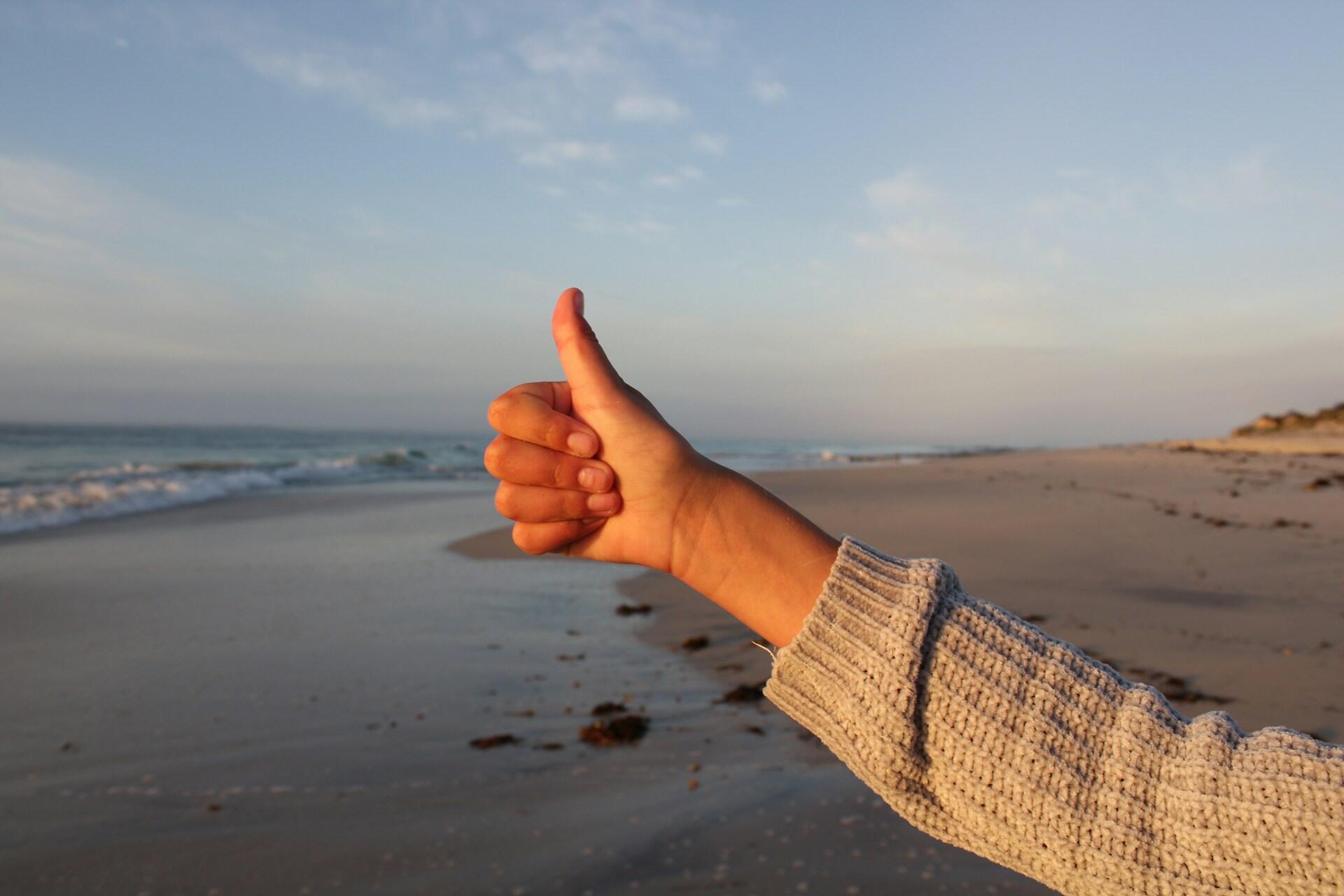 Hand giving a thumbs-up on a beach