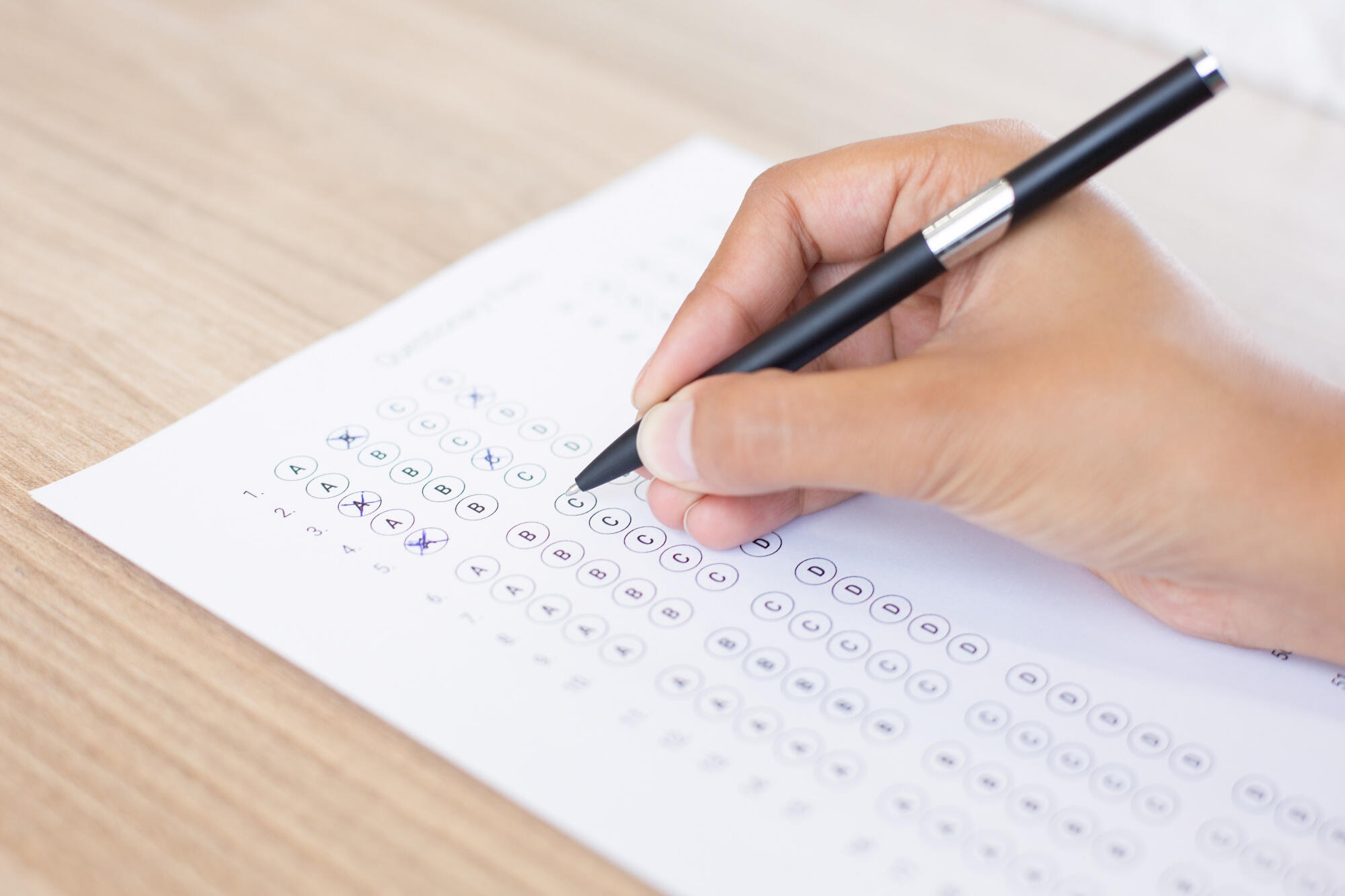 A person focused on a test, writing answers on paper with a pen in a well-lit environment.