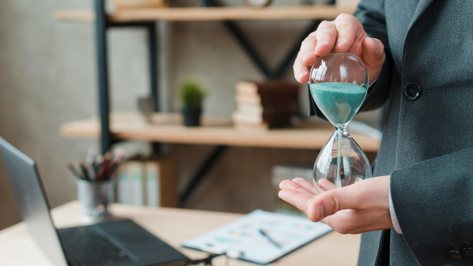 A man in a suit holds an hourglass, symbolizing the passage of time and the importance of timely decisions.