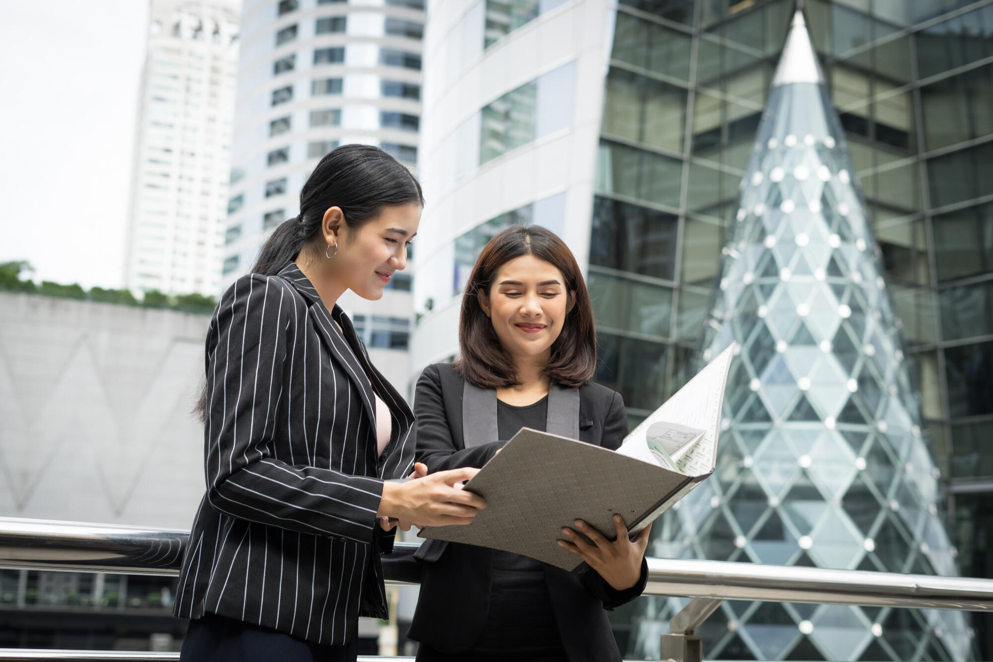 Two businesswomen reviewing a document together outside a modern office building.