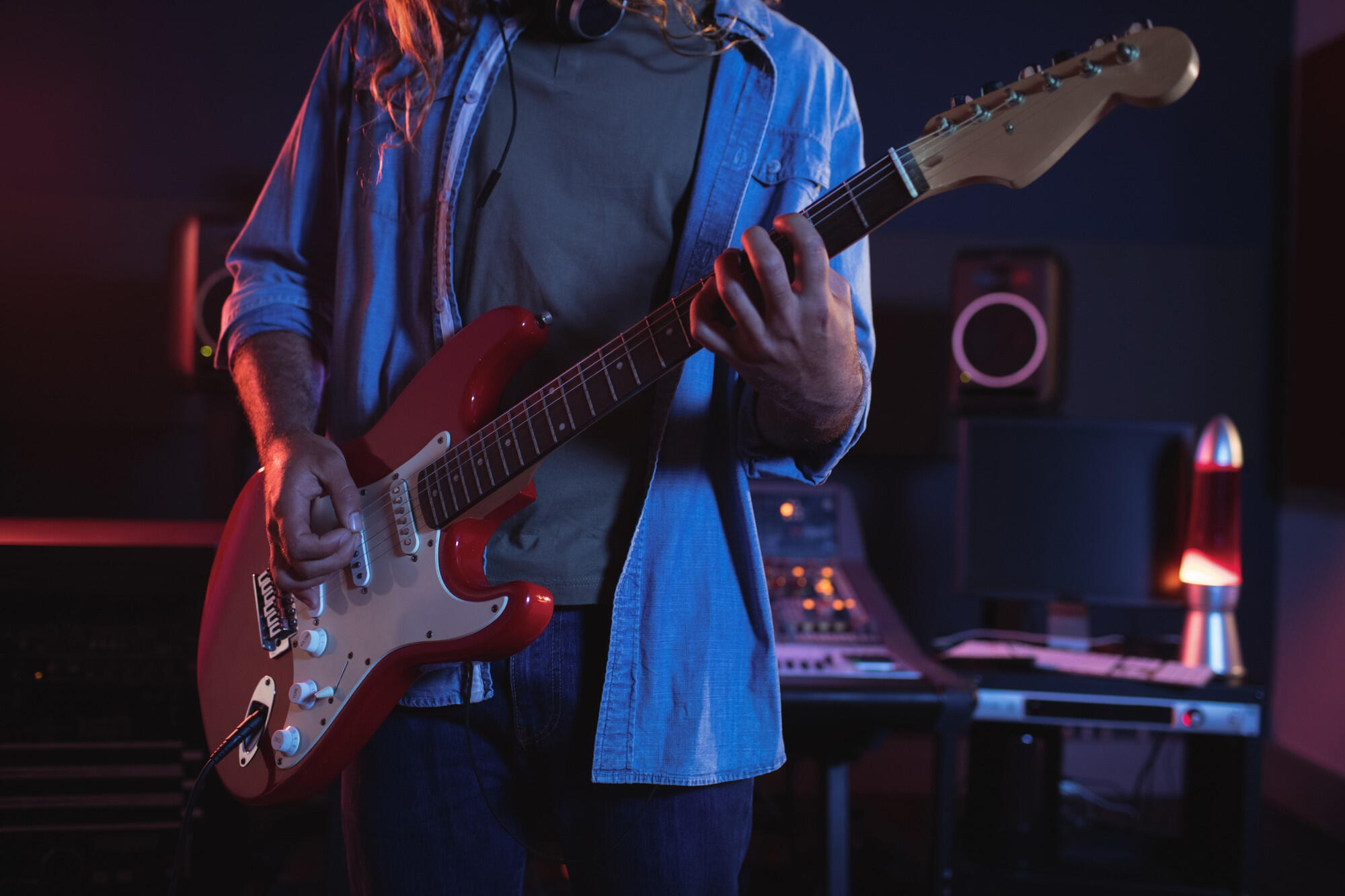 A man playing an electric guitar in a recording studio, surrounded by sound equipment and acoustic panels.