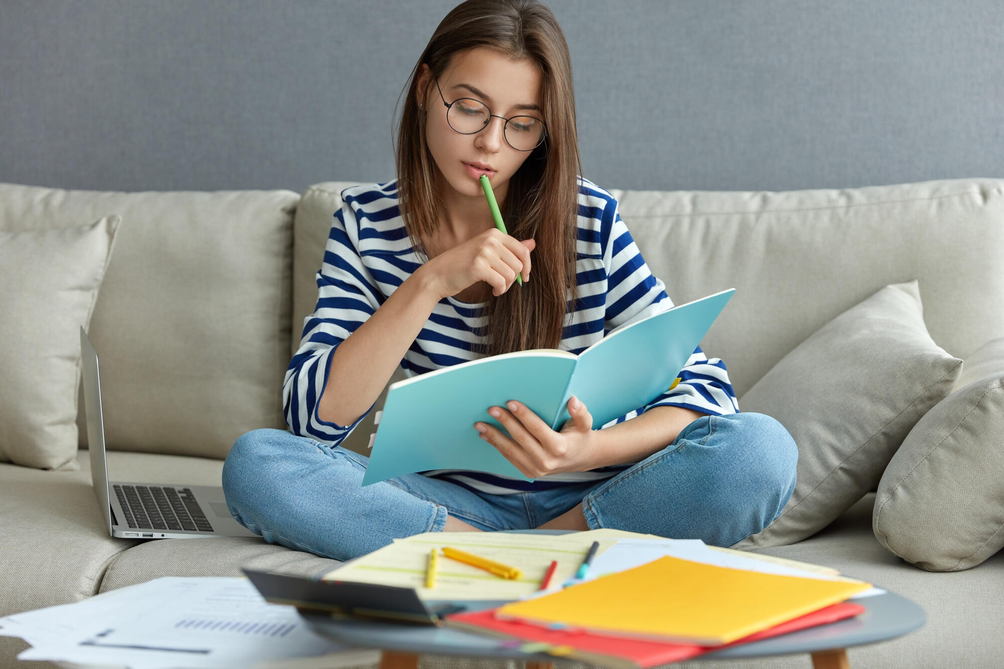 A woman sits on a couch, writing in a notebook with a pen, focused on her task.