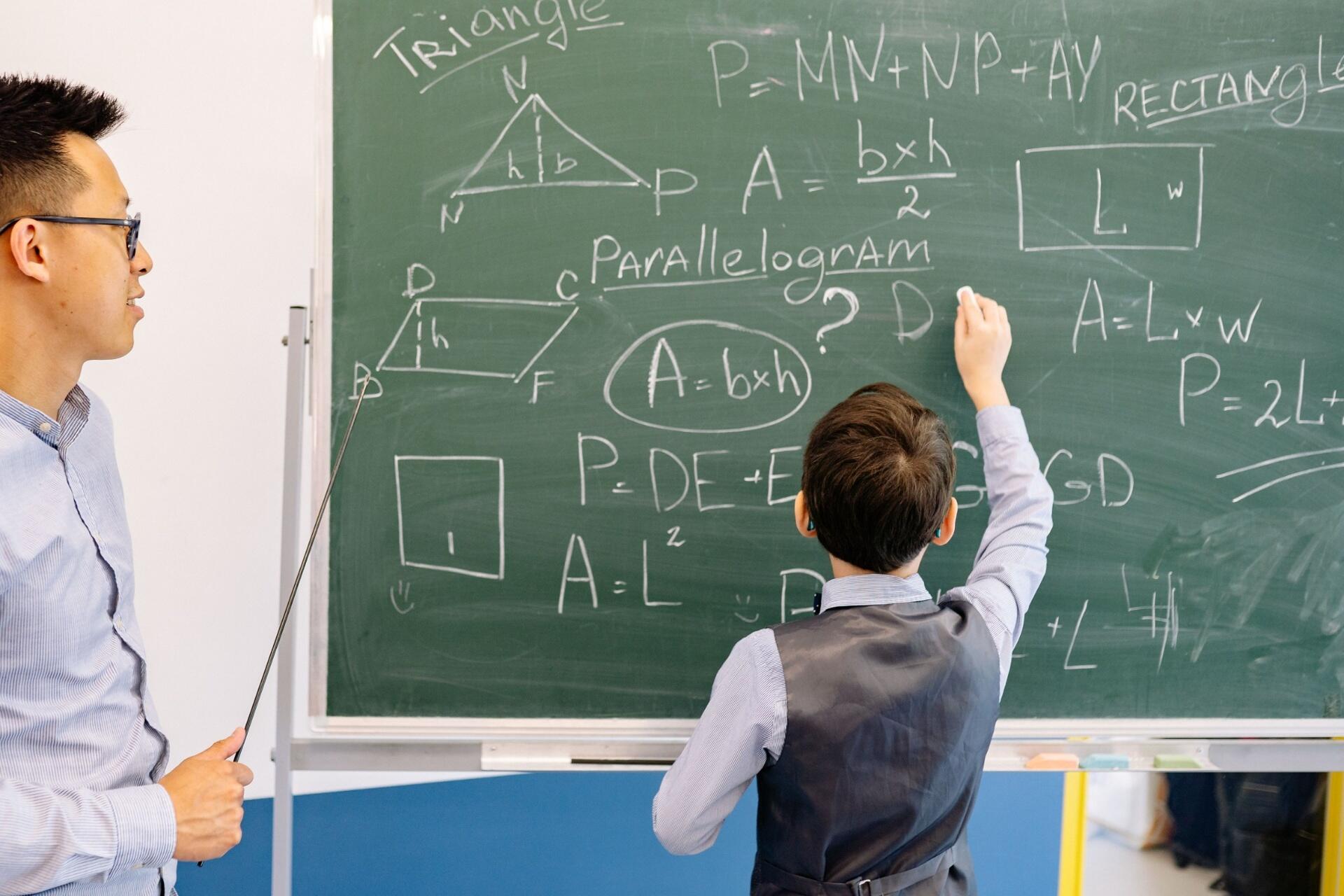 H2 Maths teacher explaining mathematical concepts on a classroom whiteboard to a student during an interactive lesson
