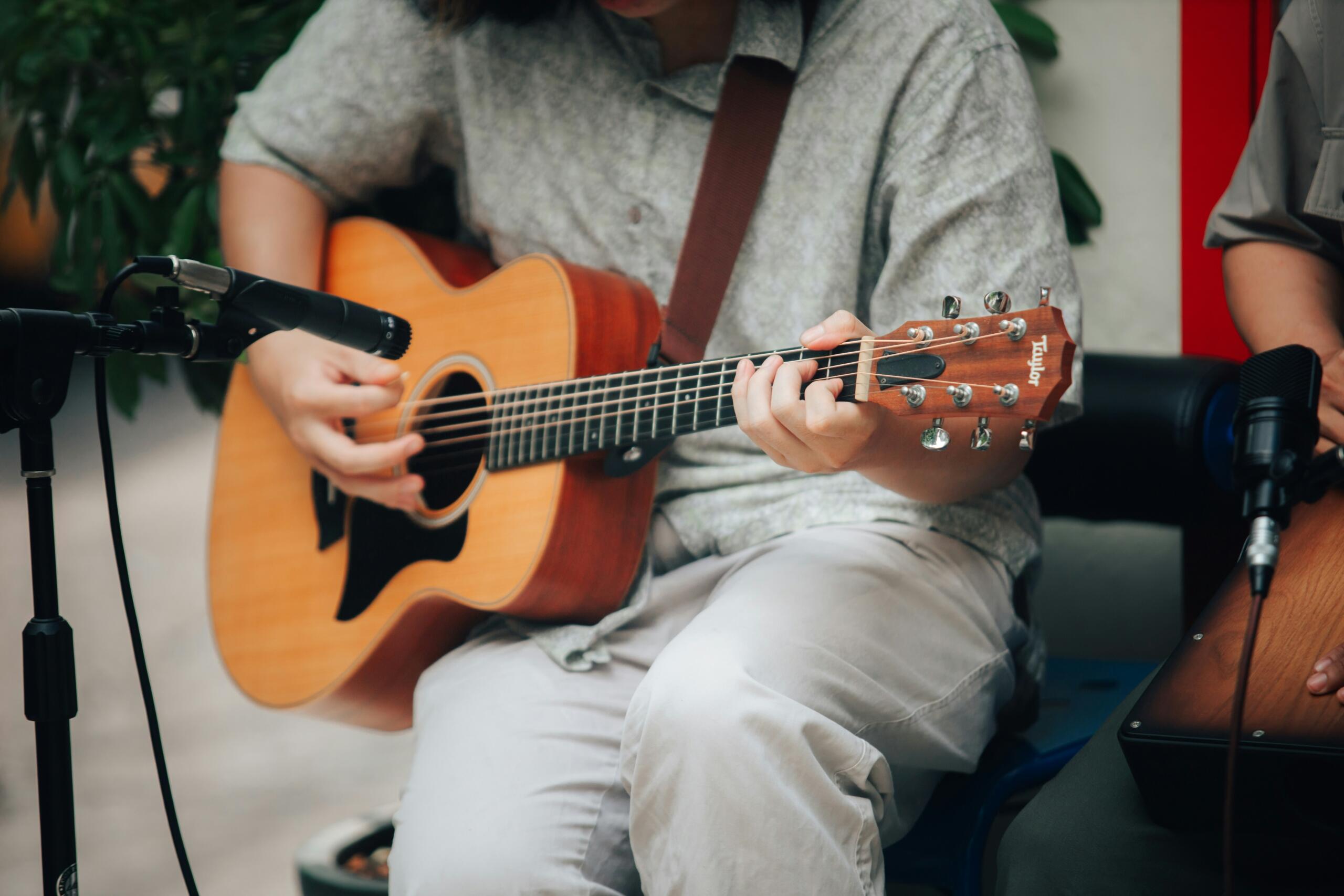 A man seated, strumming an acoustic guitar, focused on his music in a cozy indoor setting.