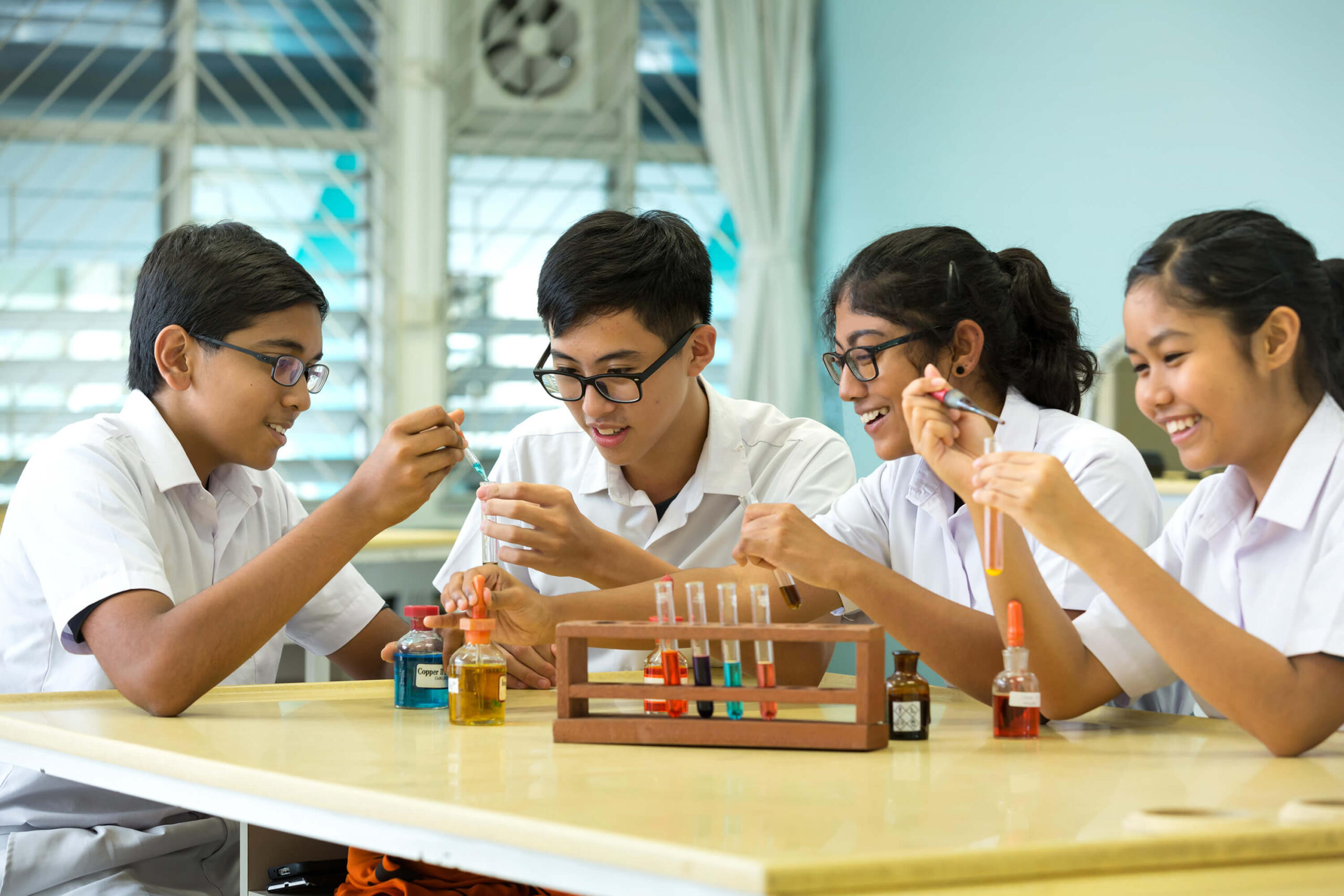 Four students in a laboratory setting, engaged in a science experiment involving test tubes and liquids.