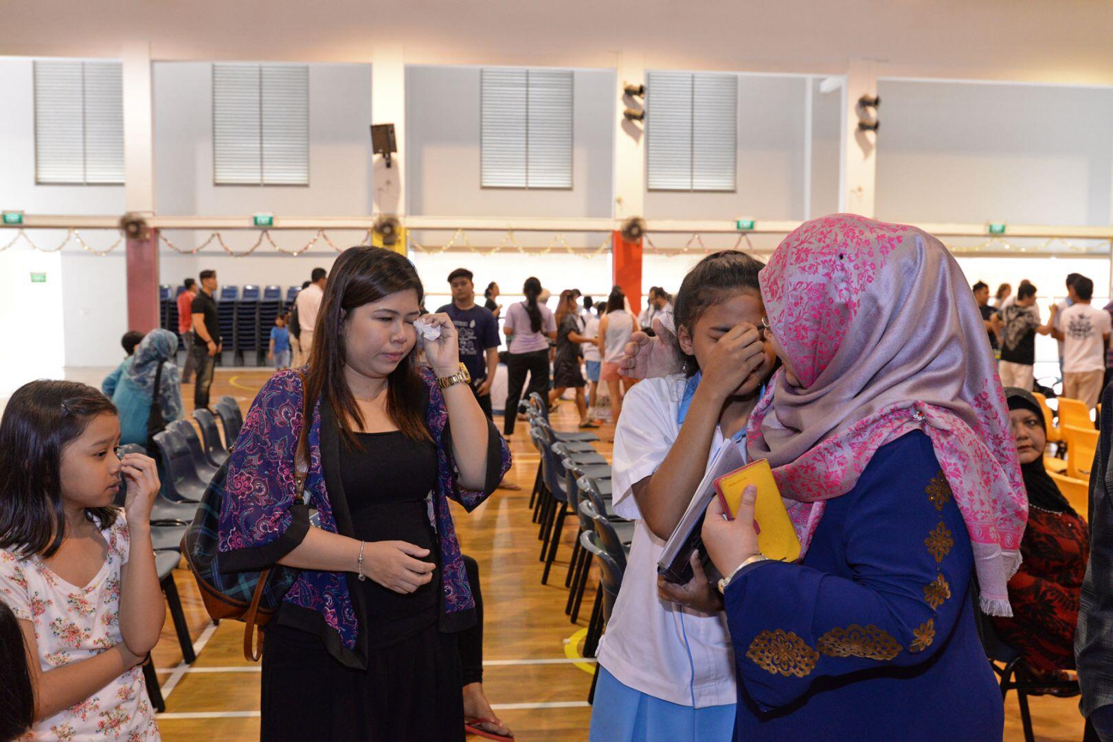 A group of people interacting in a large room with chairs, featuring two girls and a woman in a hijab engaged in conversation.