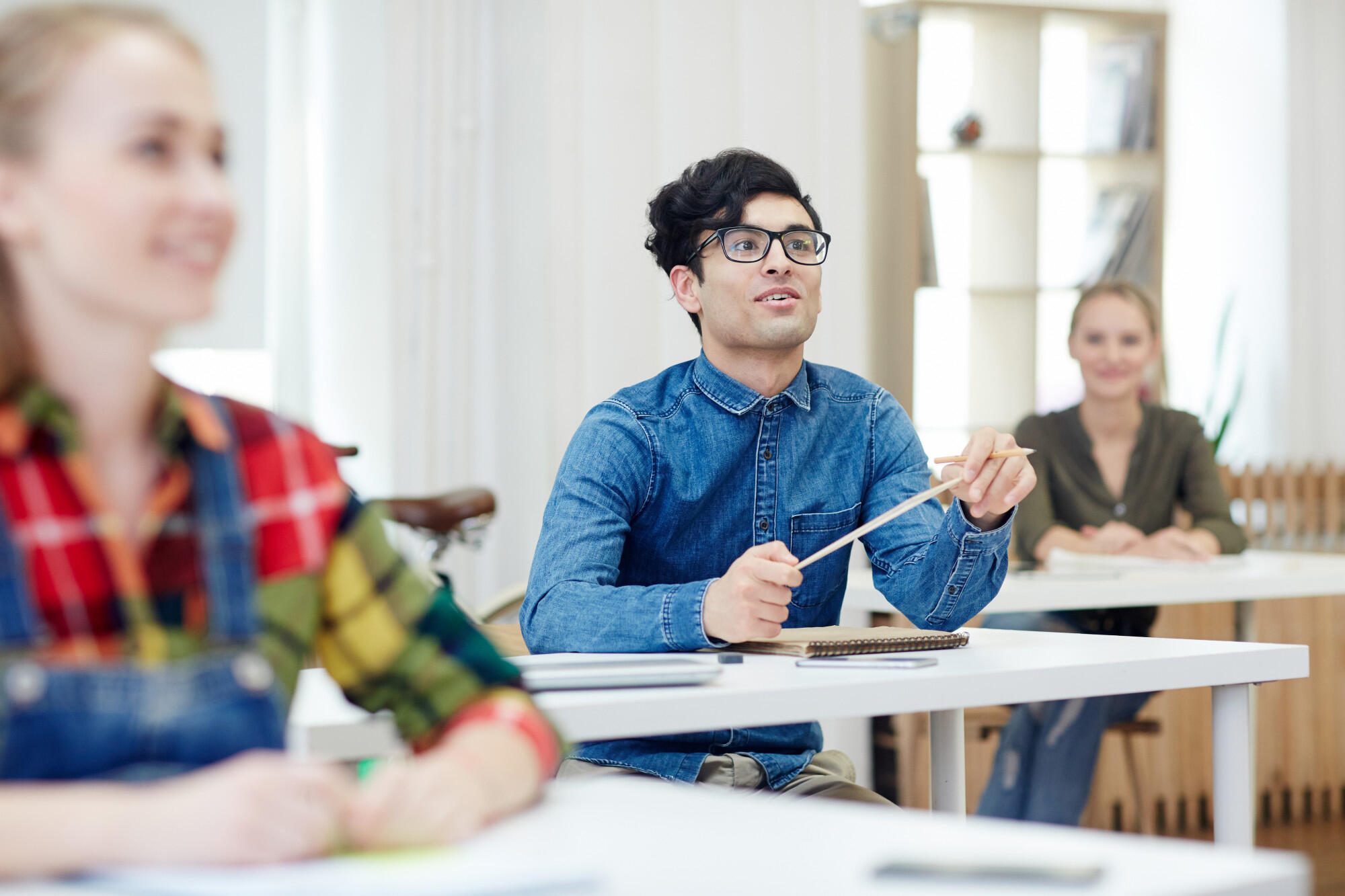 A man wearing glasses sits at a table surrounded by fellow students engaged in discussion.