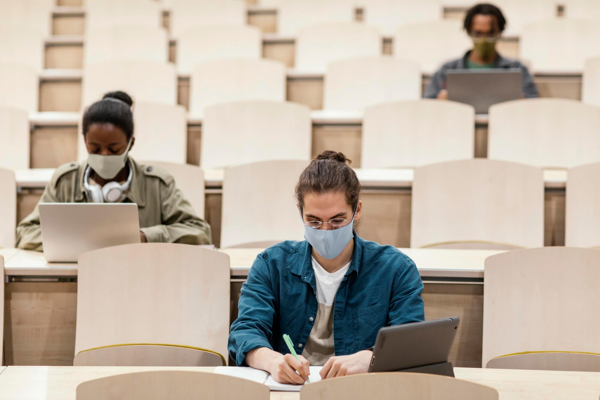 A group of students wearing face masks attentively listening in a lecture hall setting.