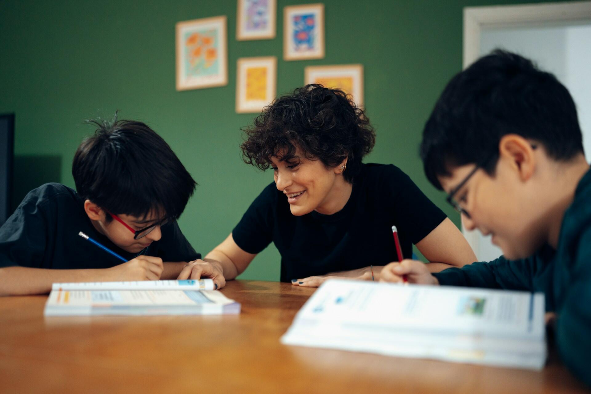 Three students studying and writing in workbooks.