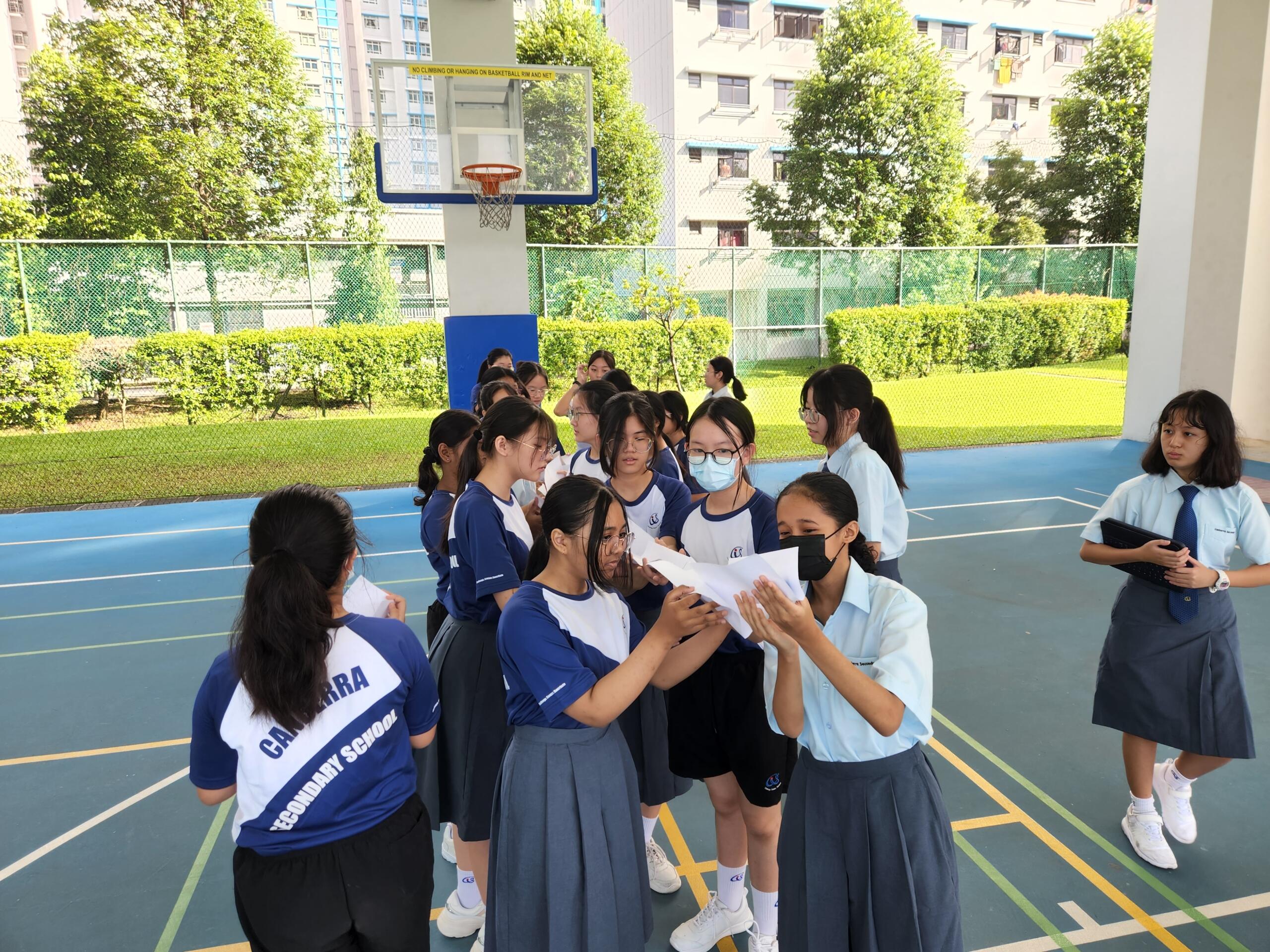 Group of students in sports uniforms collaborating on a project outdoors at a school basketball court.