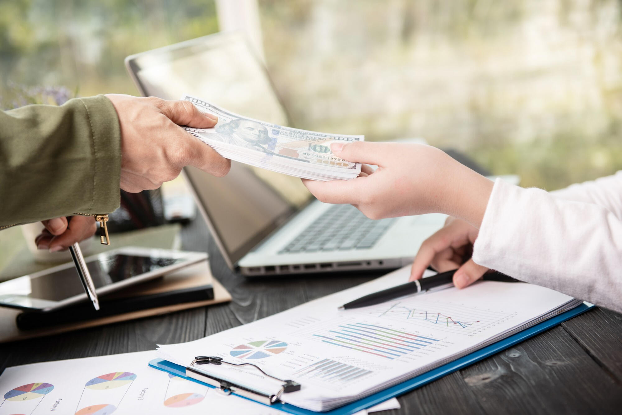 A man hands cash to another person at a desk, indicating a financial transaction or exchange.