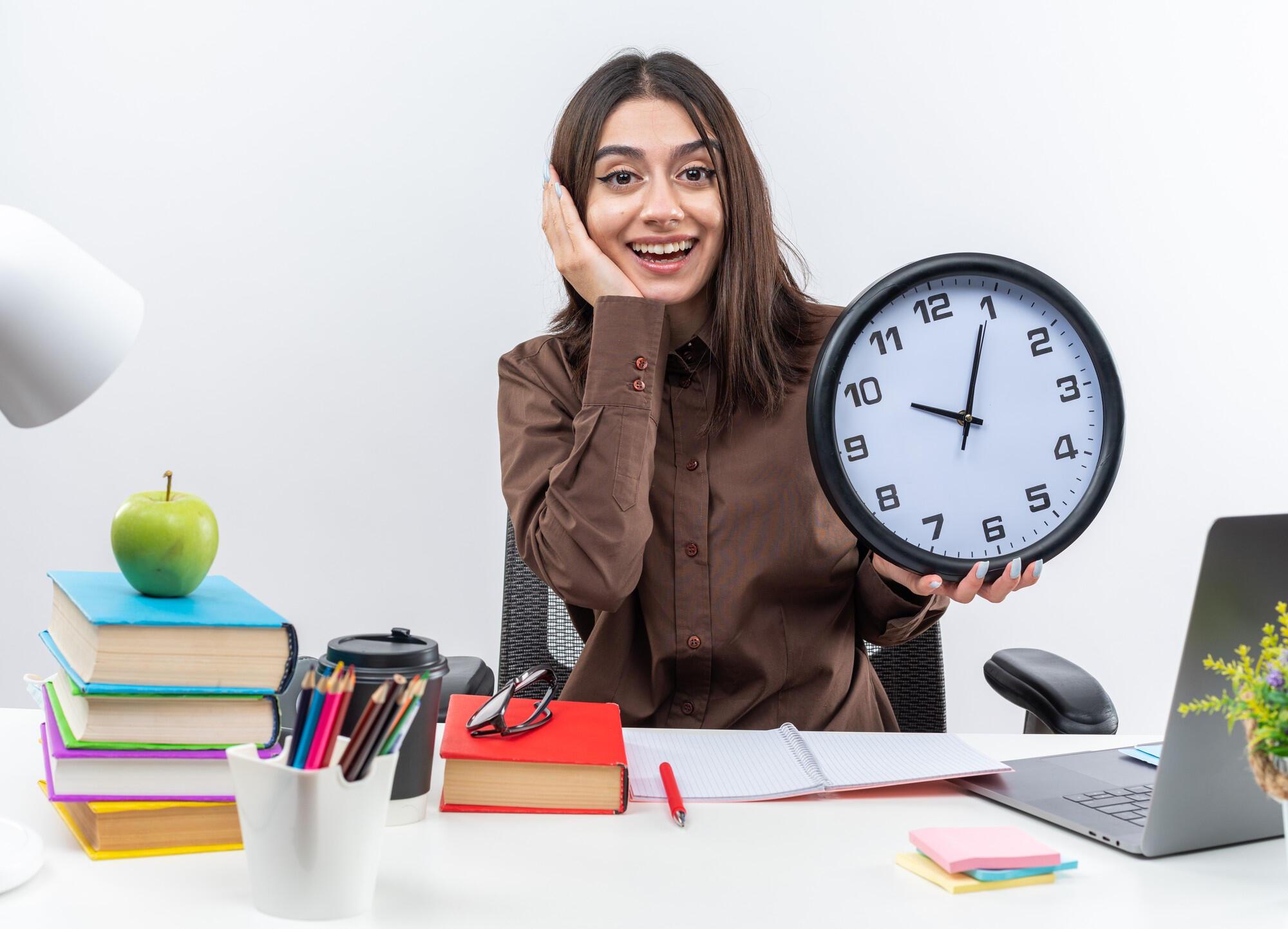 A woman seated at a desk, holding a clock, appears focused and contemplative.