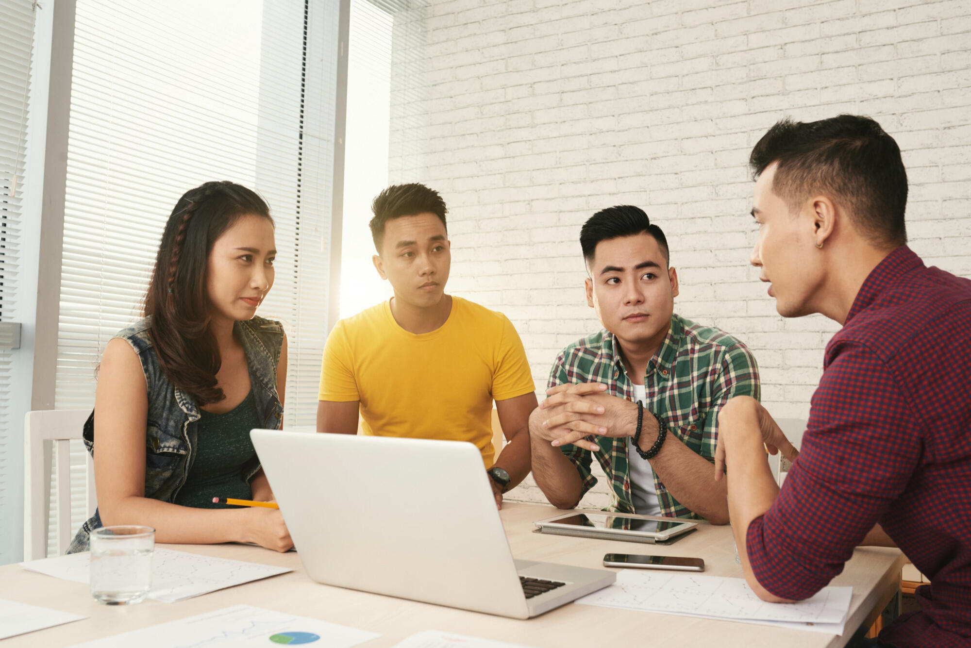 A group of Asian business professionals engaged in a discussion during a meeting, with documents and laptops on the table.