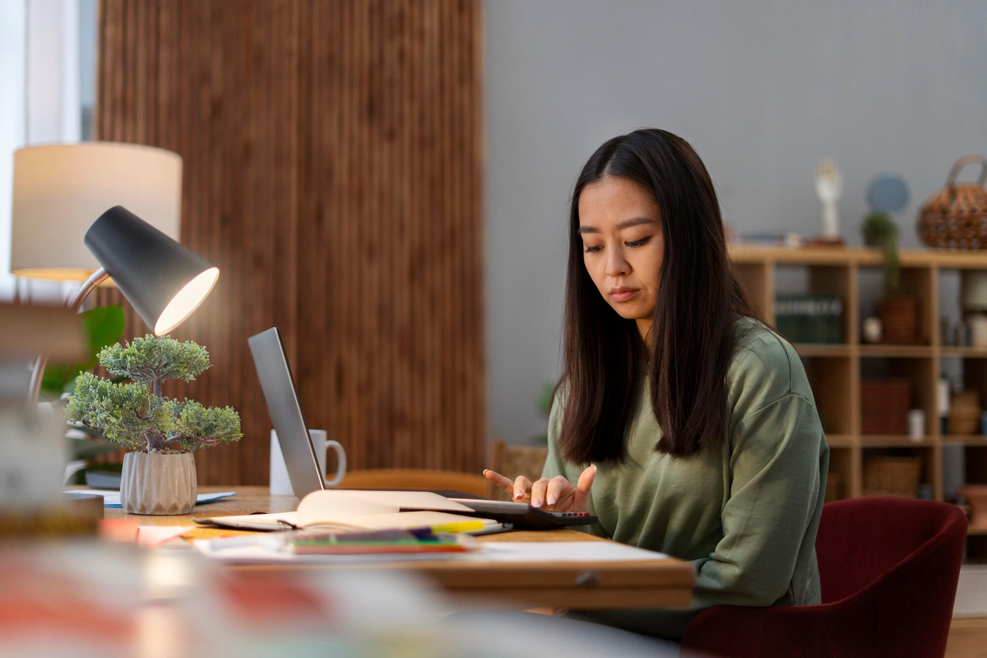 A woman seated at a desk, focused on her laptop, with a notepad and pen beside her.