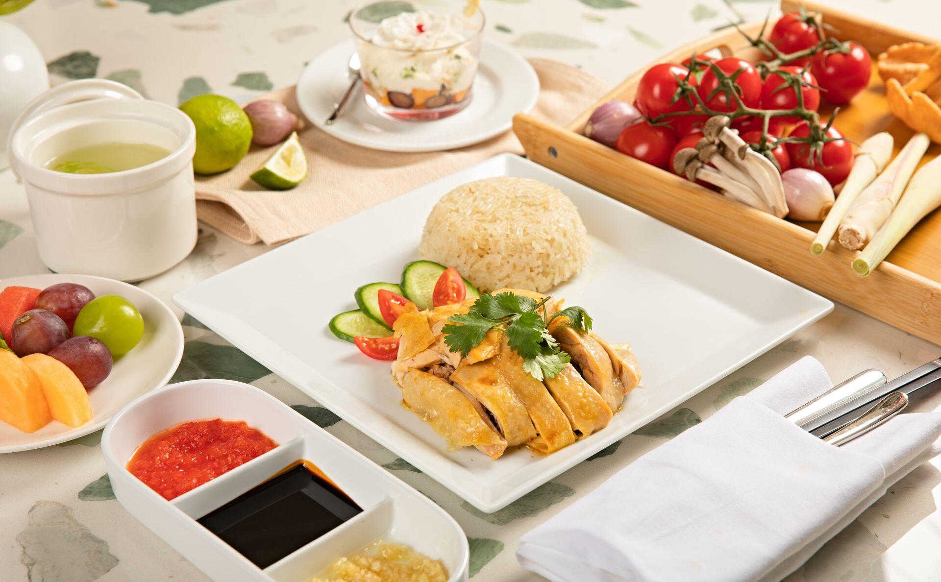 Tasty Hainanese chicken rice with fresh fruits and condiments, beautifully presented.