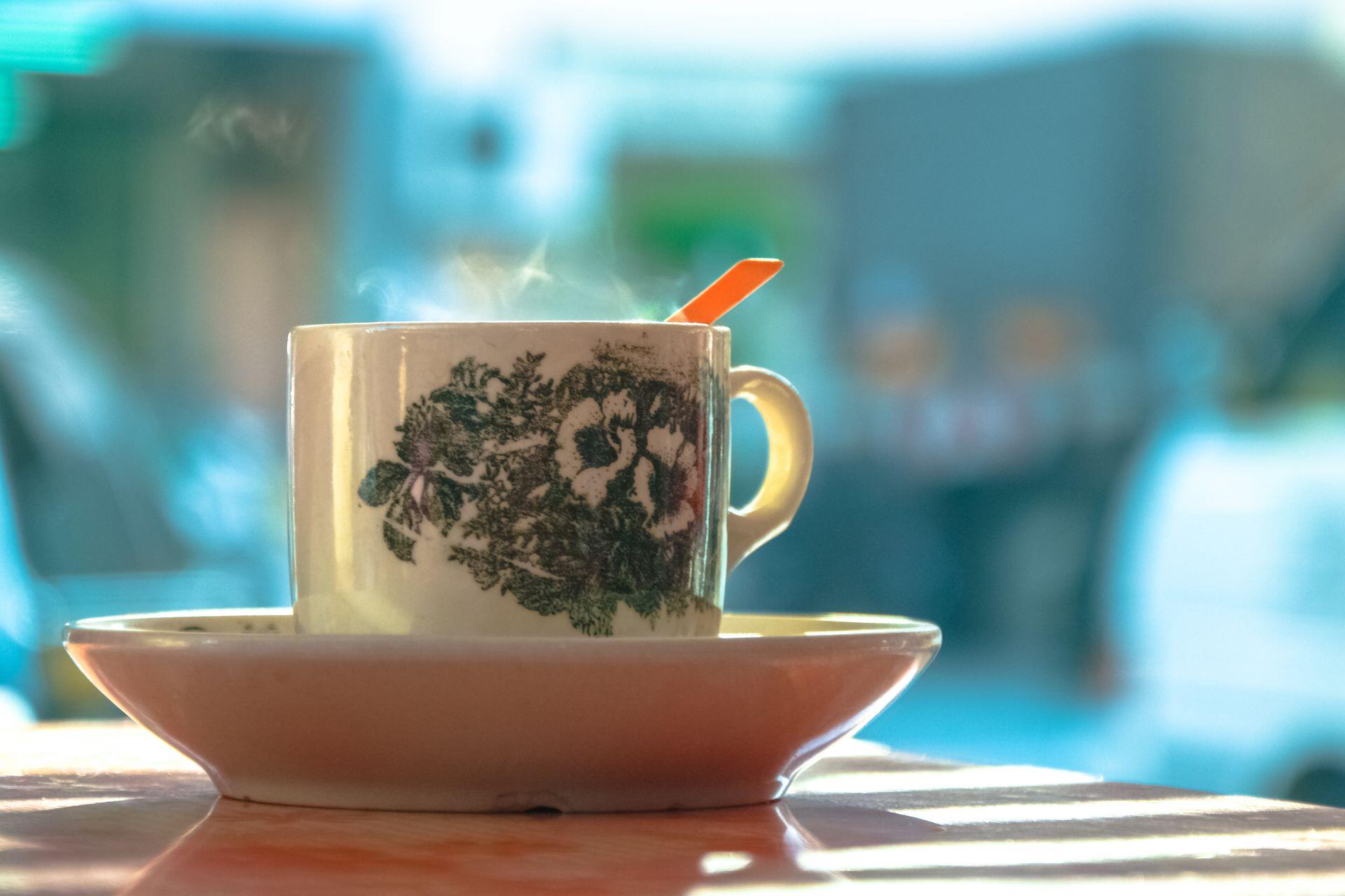 Vintage floral teacup and saucer with an orange spoon sit on a sunlit table, evoking warmth and calm against a softly blurred café background.