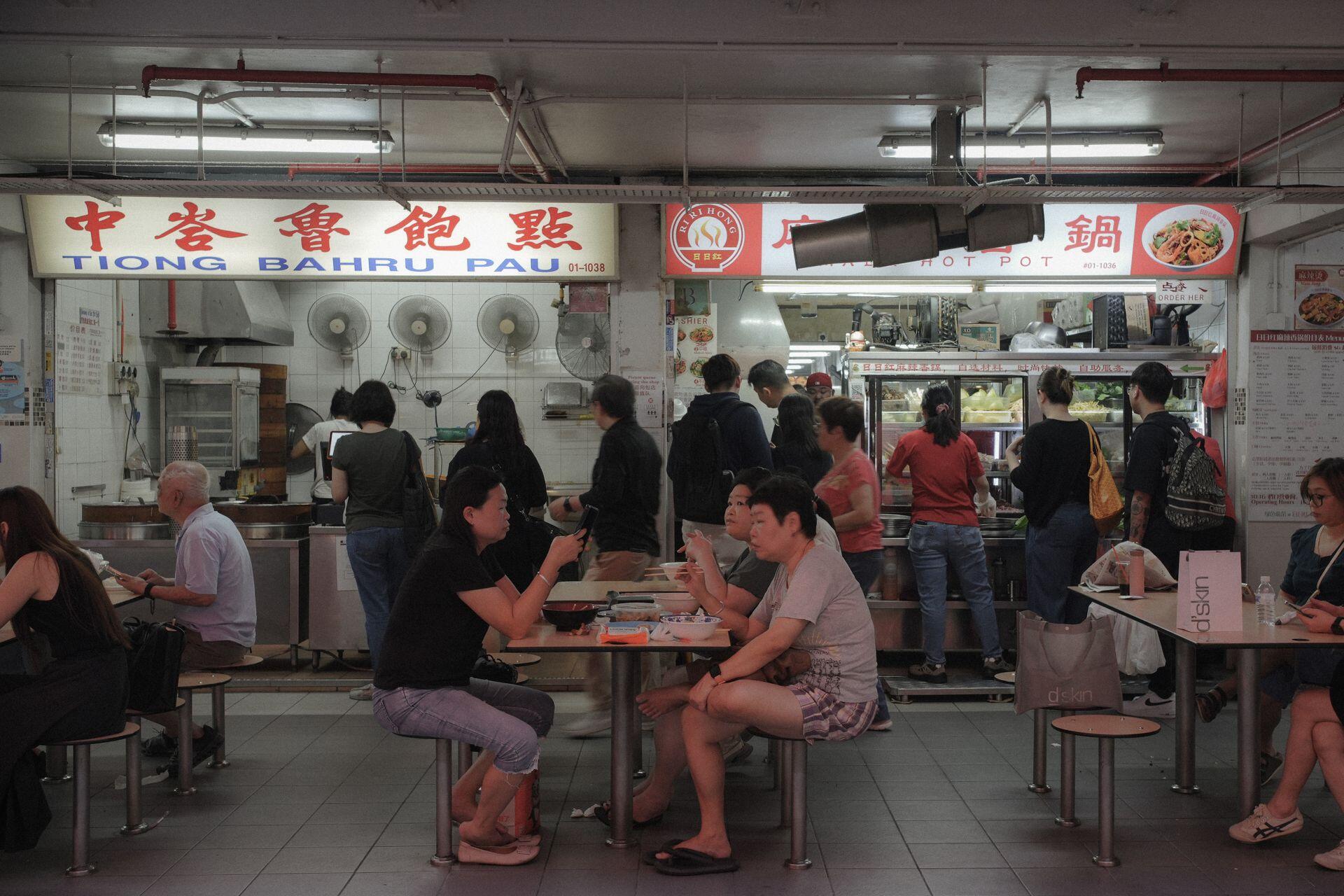 Customers enjoy diverse cuisine at Tiong Bahru Pau in a bustling Singaporean hawker center.