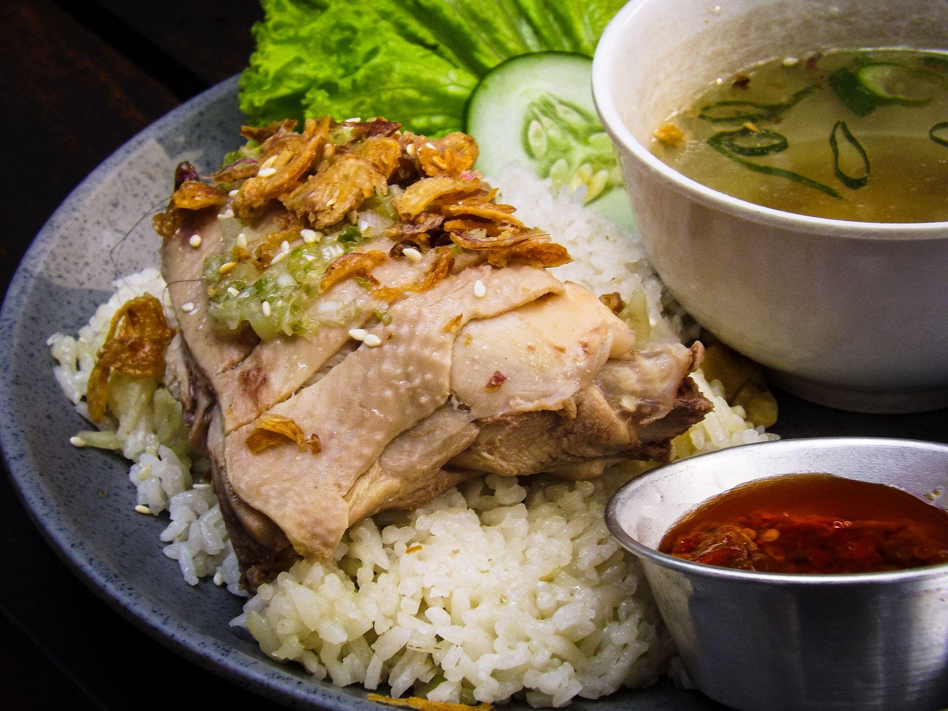 A classic dish of Hainanese chicken rice served with flavorful soup and spicy sauce