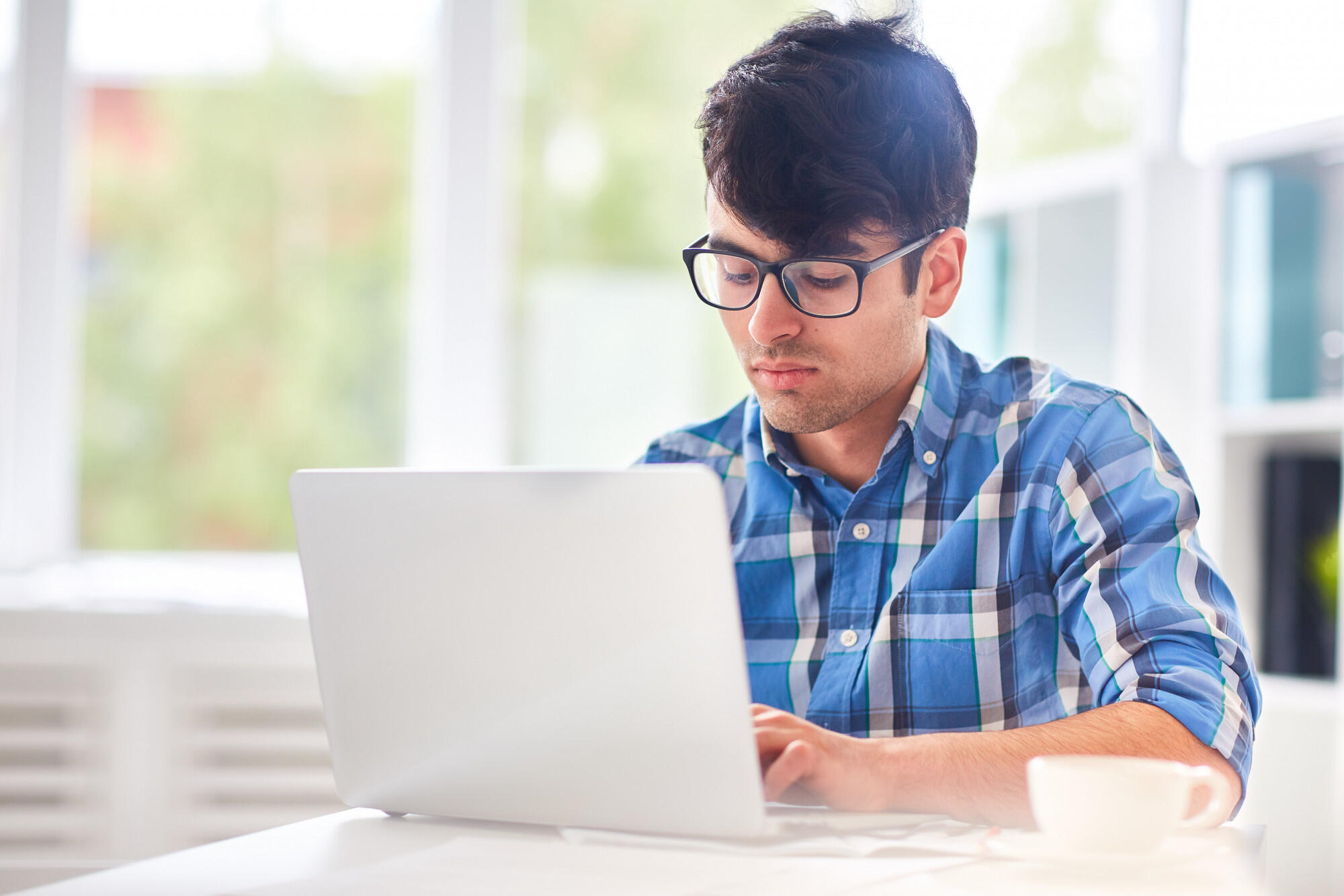 A man with glasses types on his laptop, concentrating on his work in a well-lit environment.