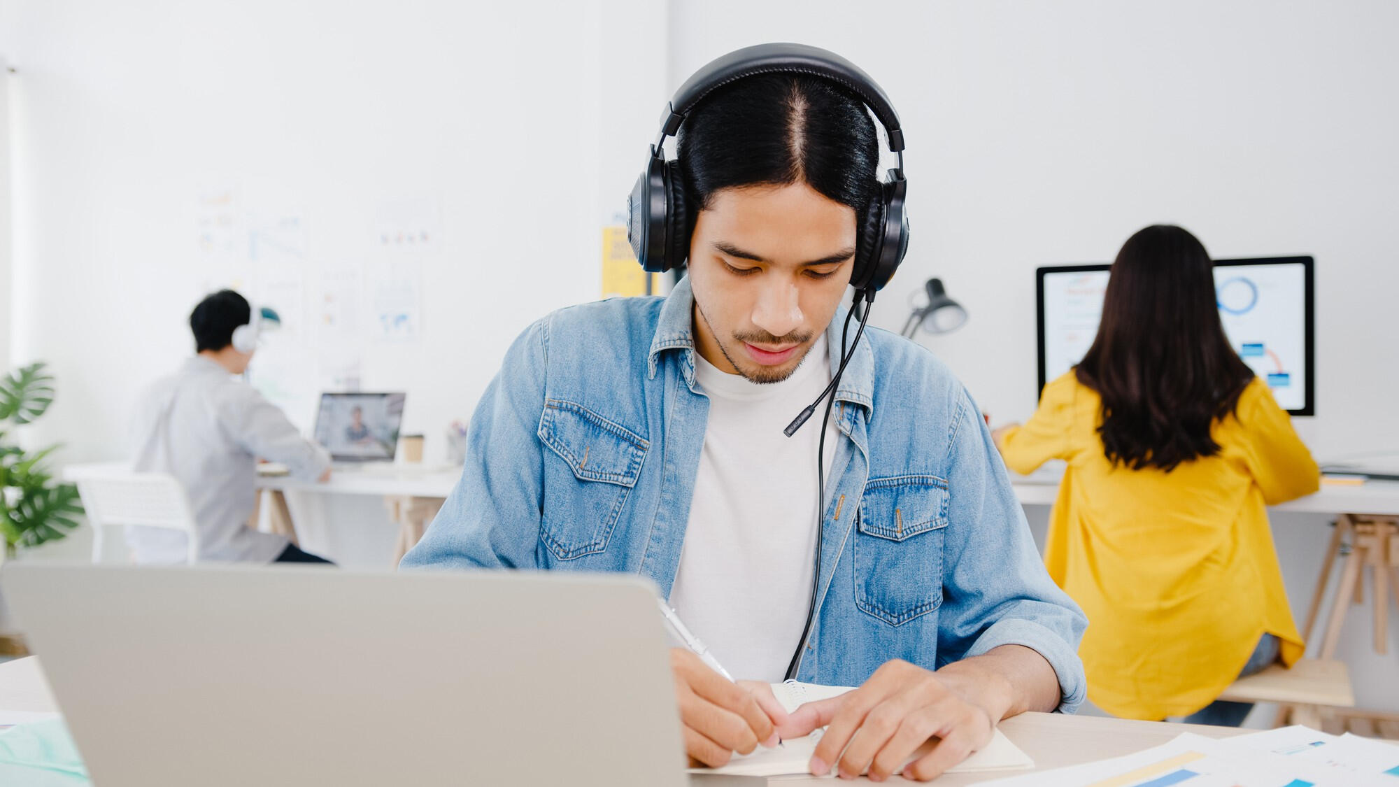 A man wearing headphones is focused on his laptop, engaged in work at a desk.