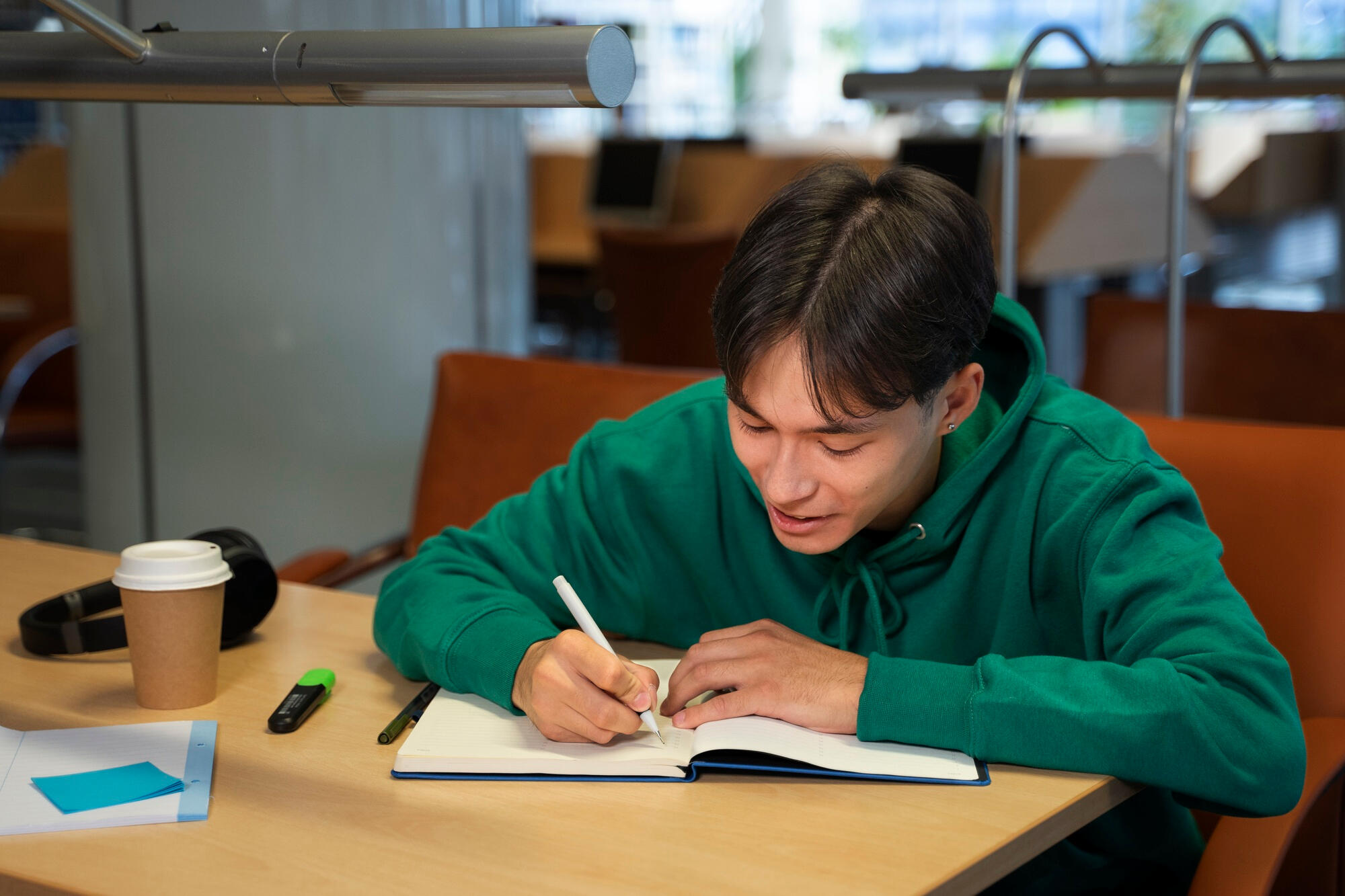 A man diligently writing notes in a notebook, surrounded by a few books and a cup of coffee.