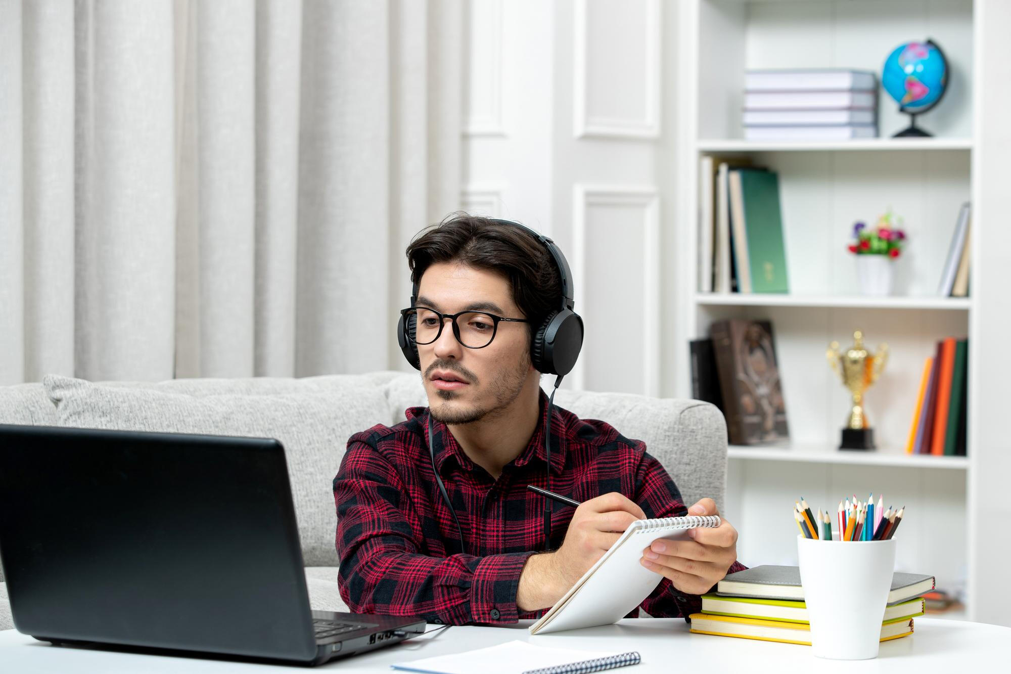 A man with headphones sits at a desk, focused on his laptop, engaged in work or a virtual meeting.