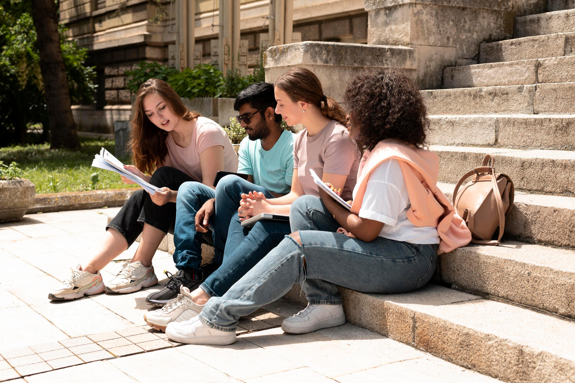 Four young people sitting on steps, engaged in reading a book together, sharing ideas and enjoying each other's company.
