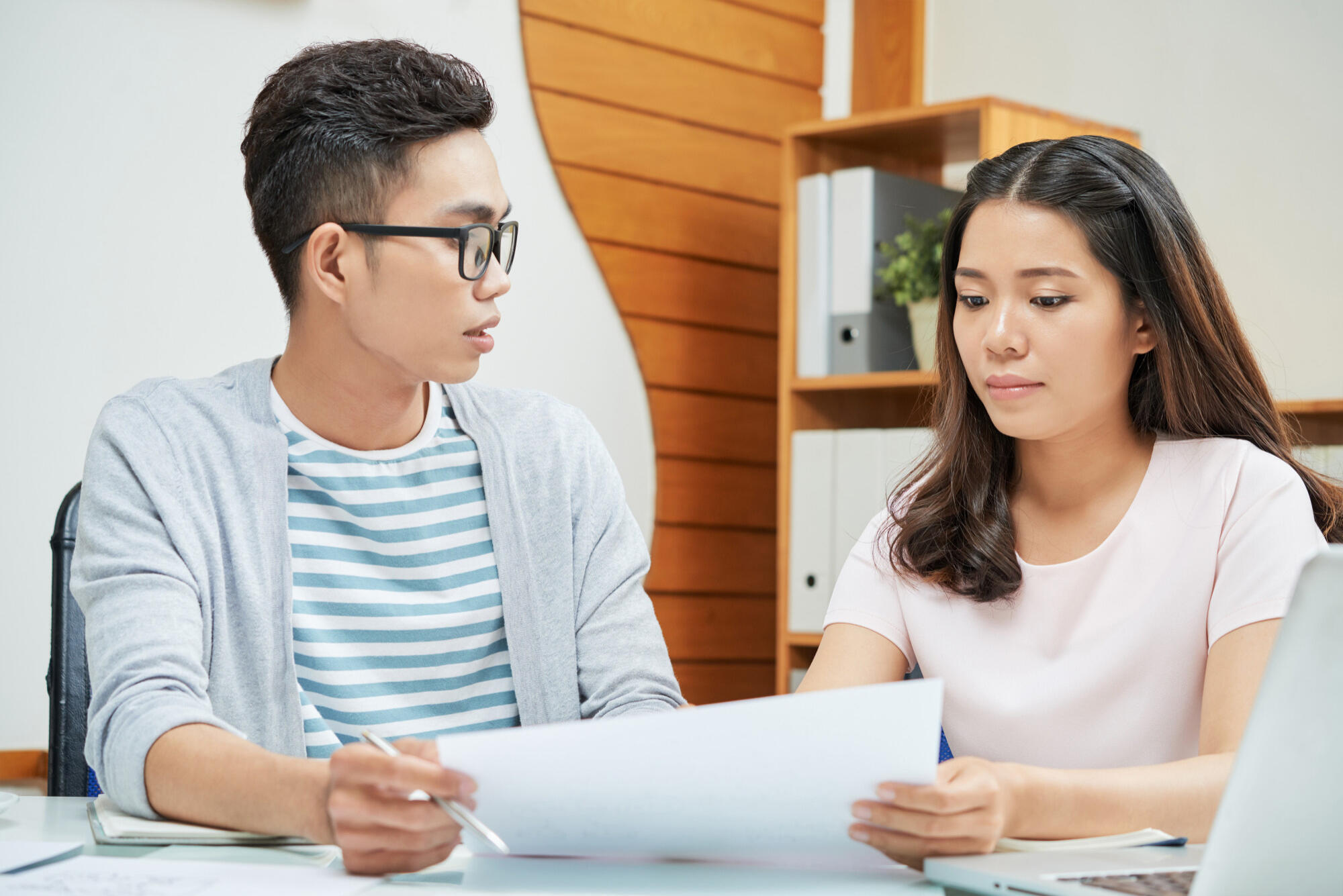 Asian couple engaged in a discussion, reviewing a business plan together at a table with documents and a laptop.