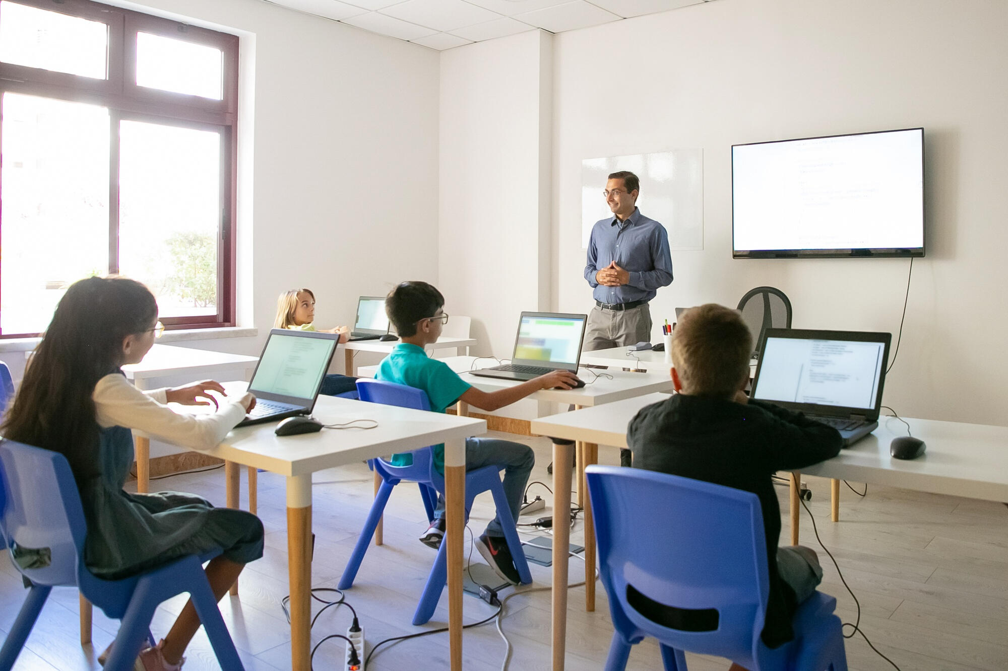 A man instructs children on computer usage in a classroom setting, fostering digital skills and engagement.