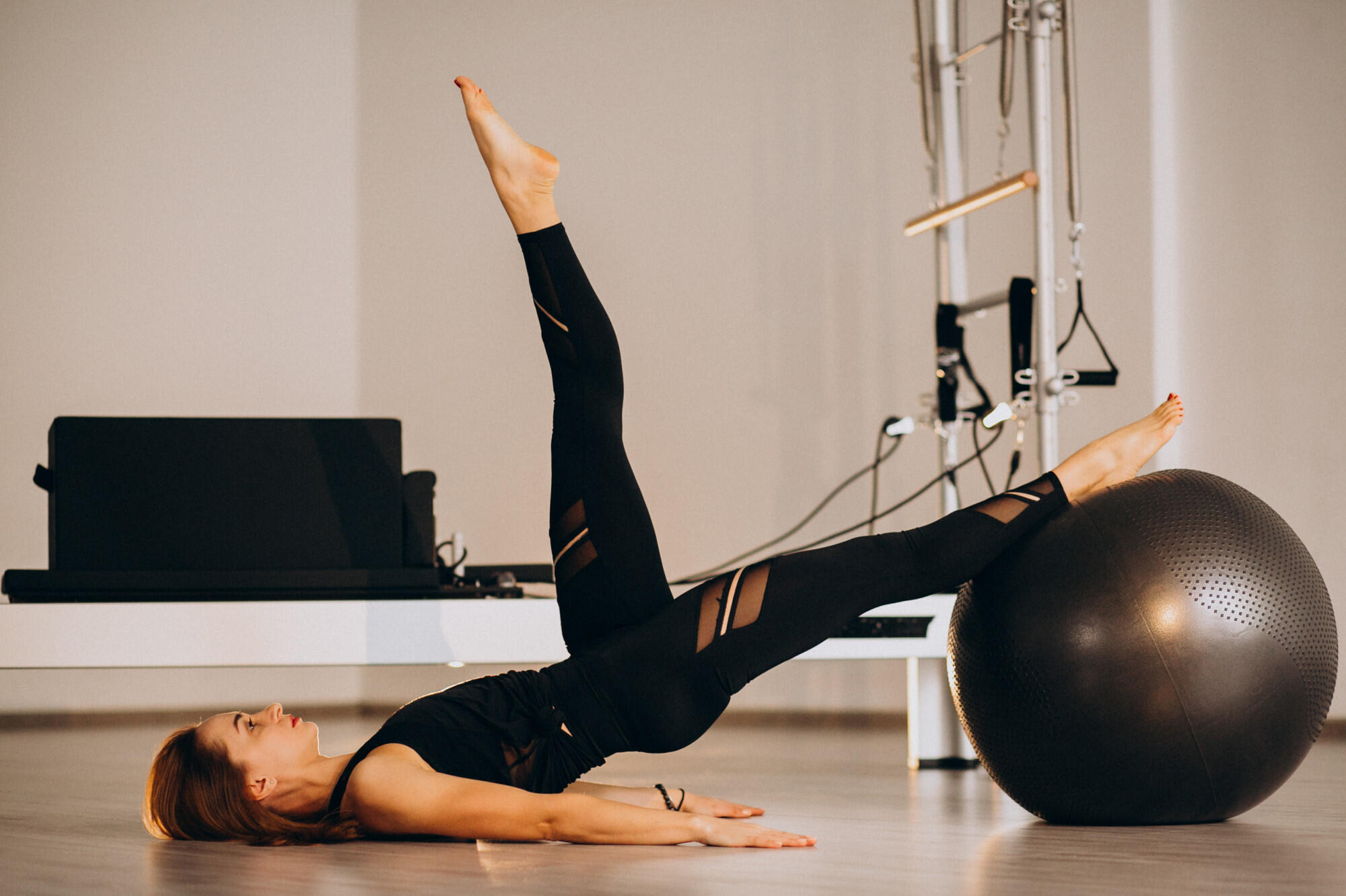 A woman performs pilates exercises on a large exercise ball, focusing on balance and core strength.
