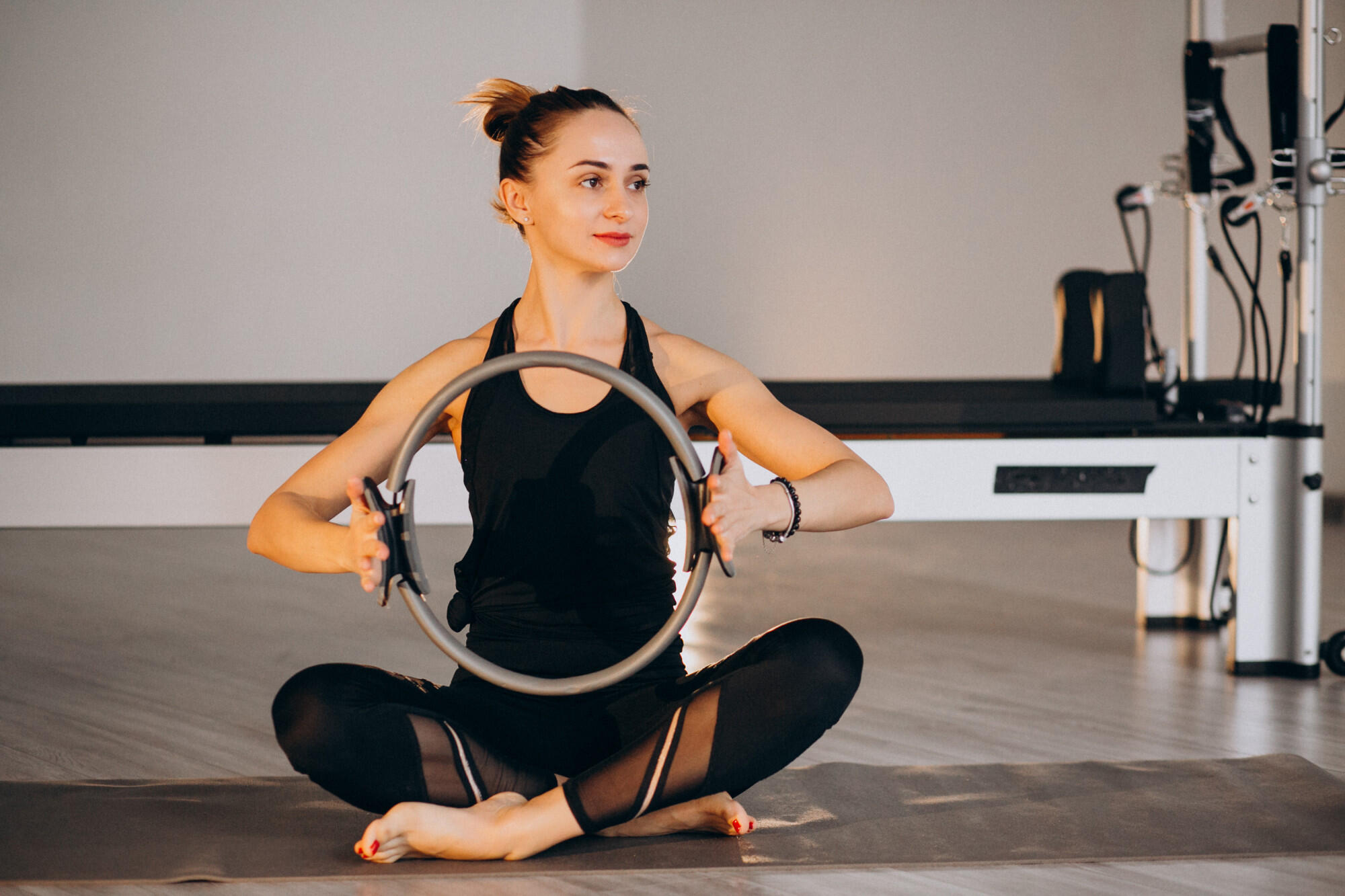 A woman performs pilates exercises using a ring, focusing on her core strength and flexibility.