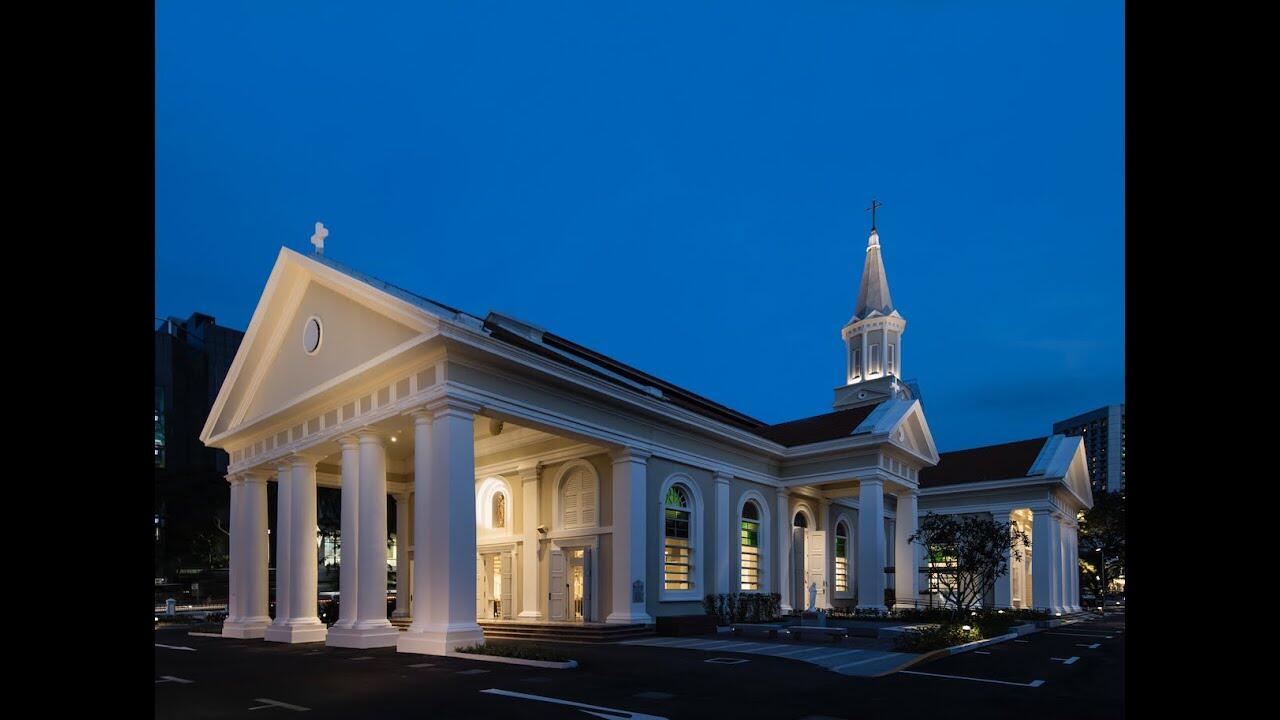 Nighttime exterior view of the illuminated Cathedral of the Good Shepherd, showing its white Renaissance-style portico with columns, red-tiled roof, and a spire topped with a cross.