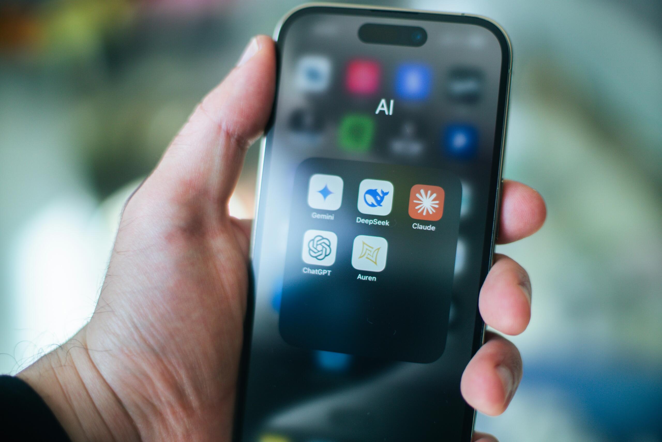 Close-up of a hand holding an iPhone, showcasing multiple app icons on its display.