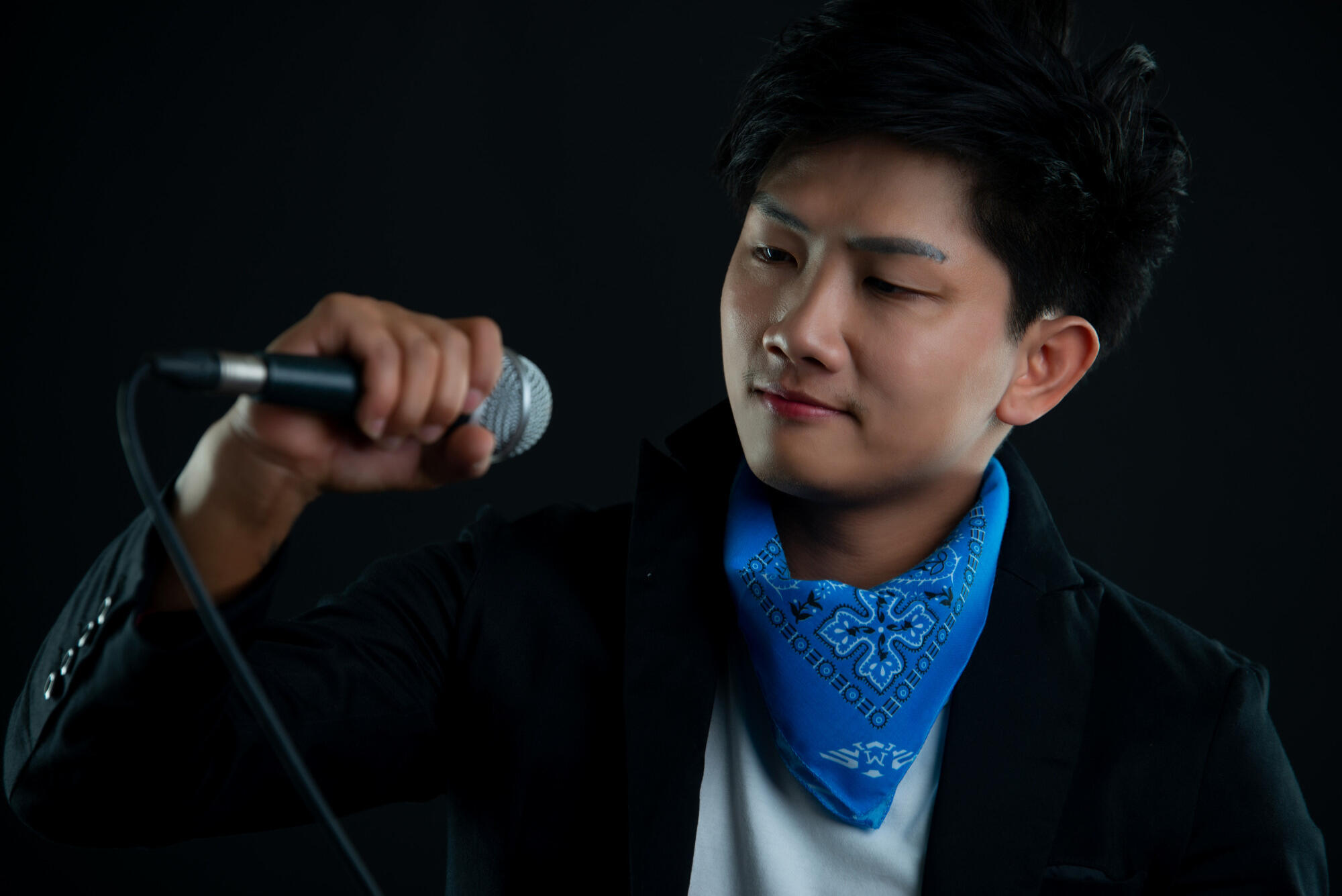 Asian male vocalist performing into a microphone, showcasing enthusiasm and energy during a live music event.