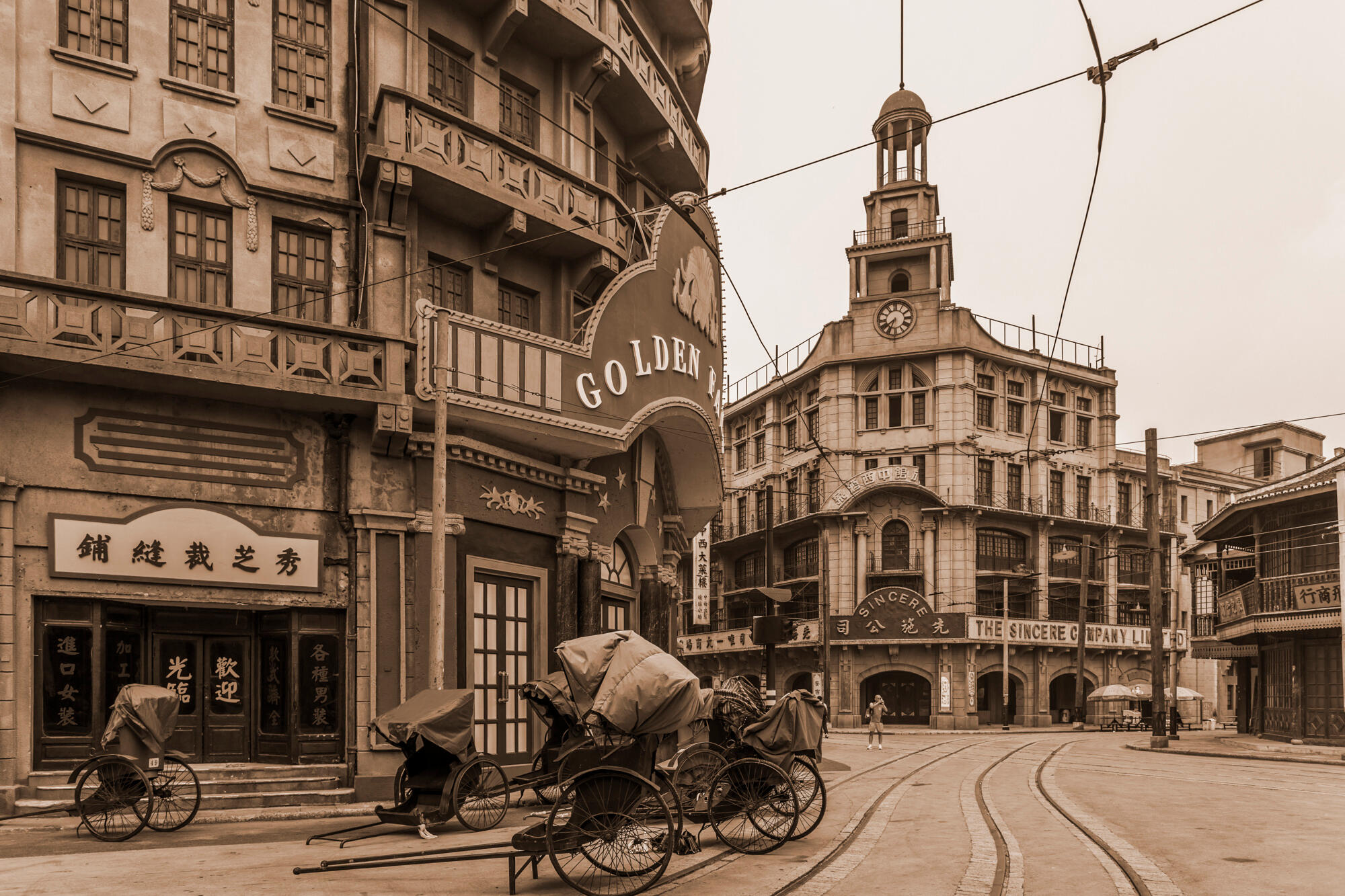 A black and white photograph depicting a bustling street scene with pedestrians and vintage cars.