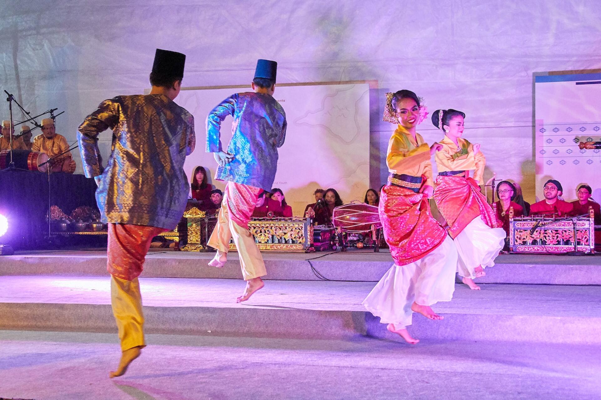 A diverse group of dancers performing energetically on stage, showcasing various dance styles and colorful costumes.