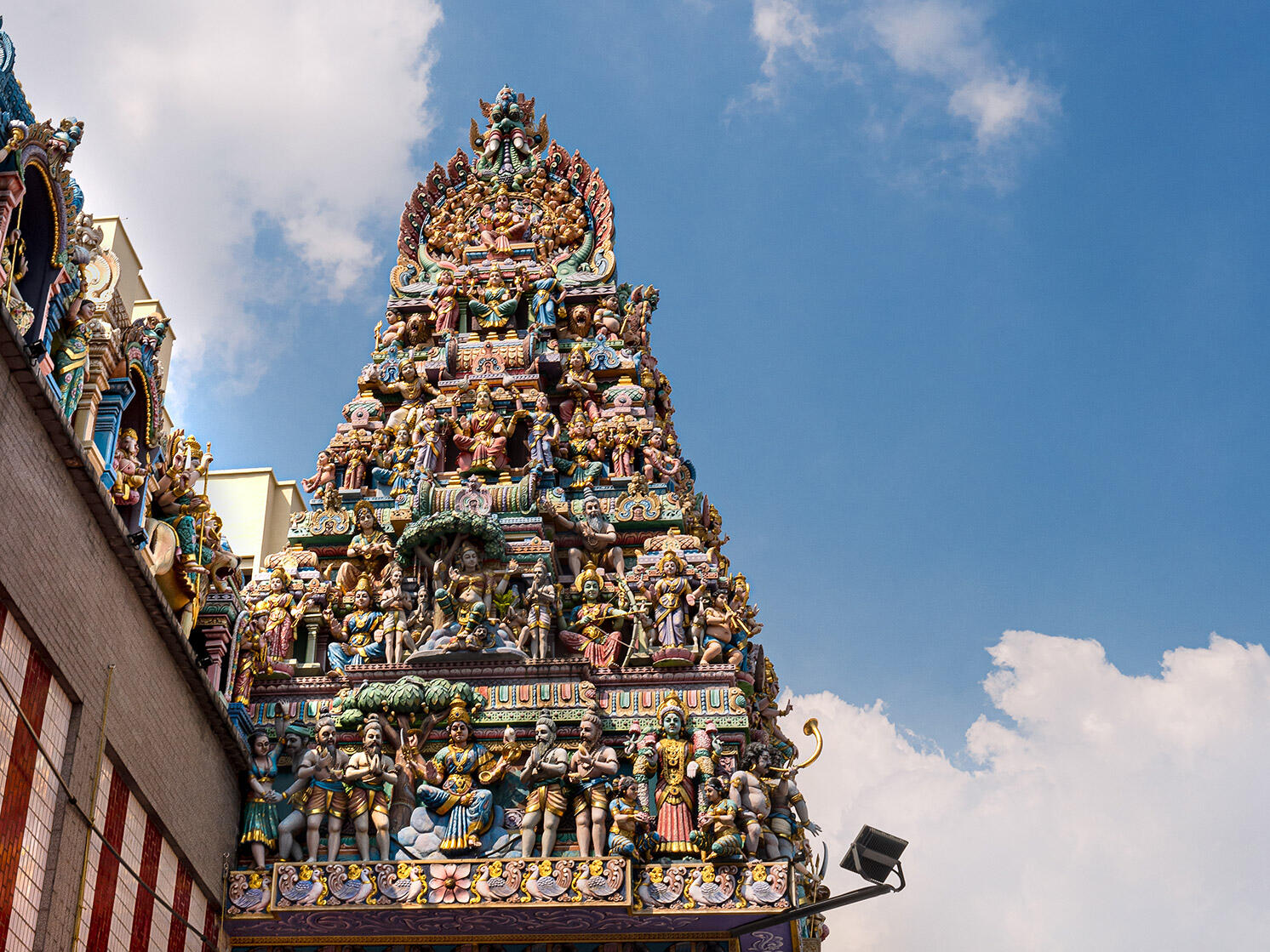 Low-angle view of the colorful gopuram tower at Sri Mariamman Temple, featuring multi-tiered sculptures of Hindu deities set against a blue sky.